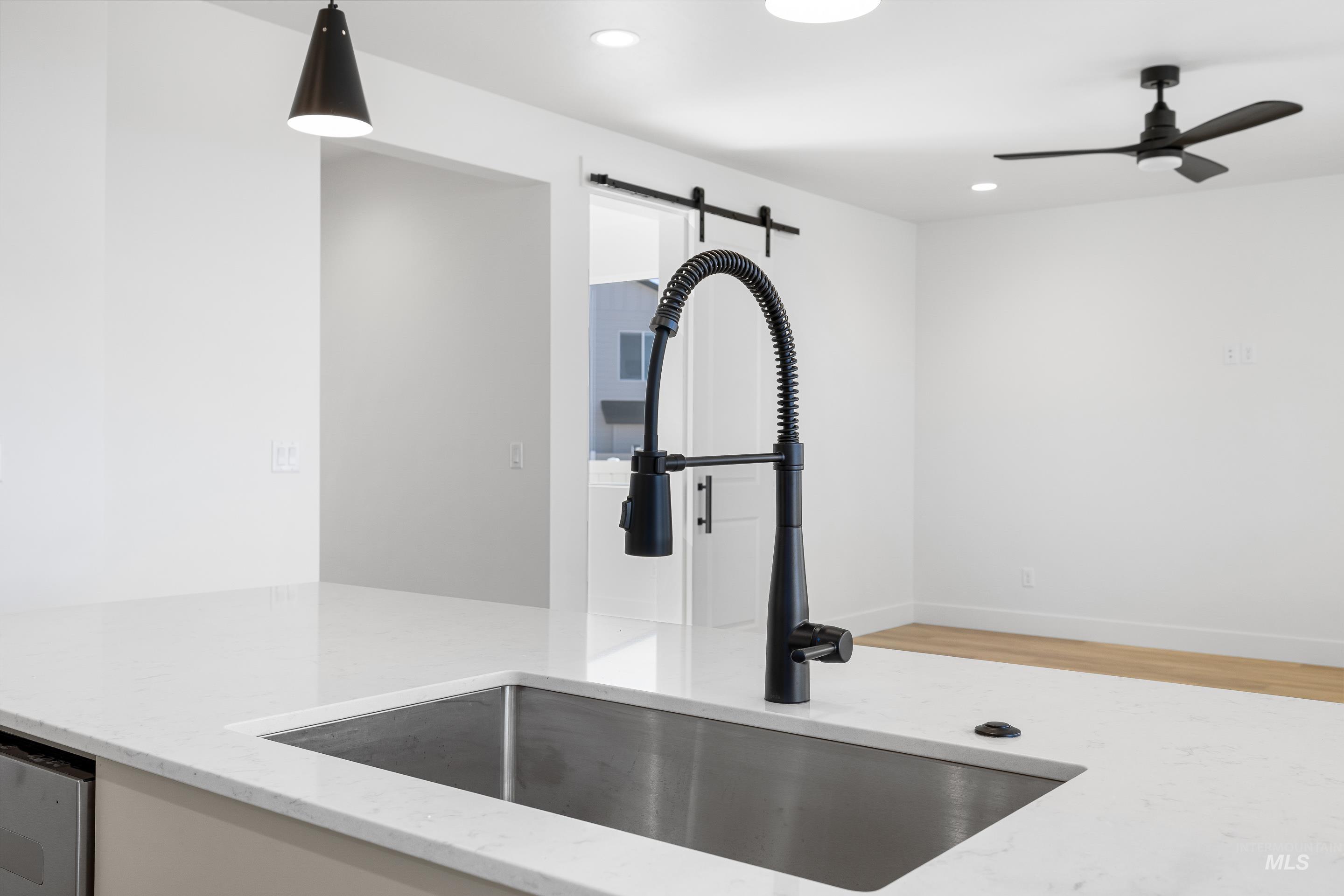 Kitchen view of light stone counters, light wood finished floors, recessed lighting, a ceiling fan, and pendant lighting