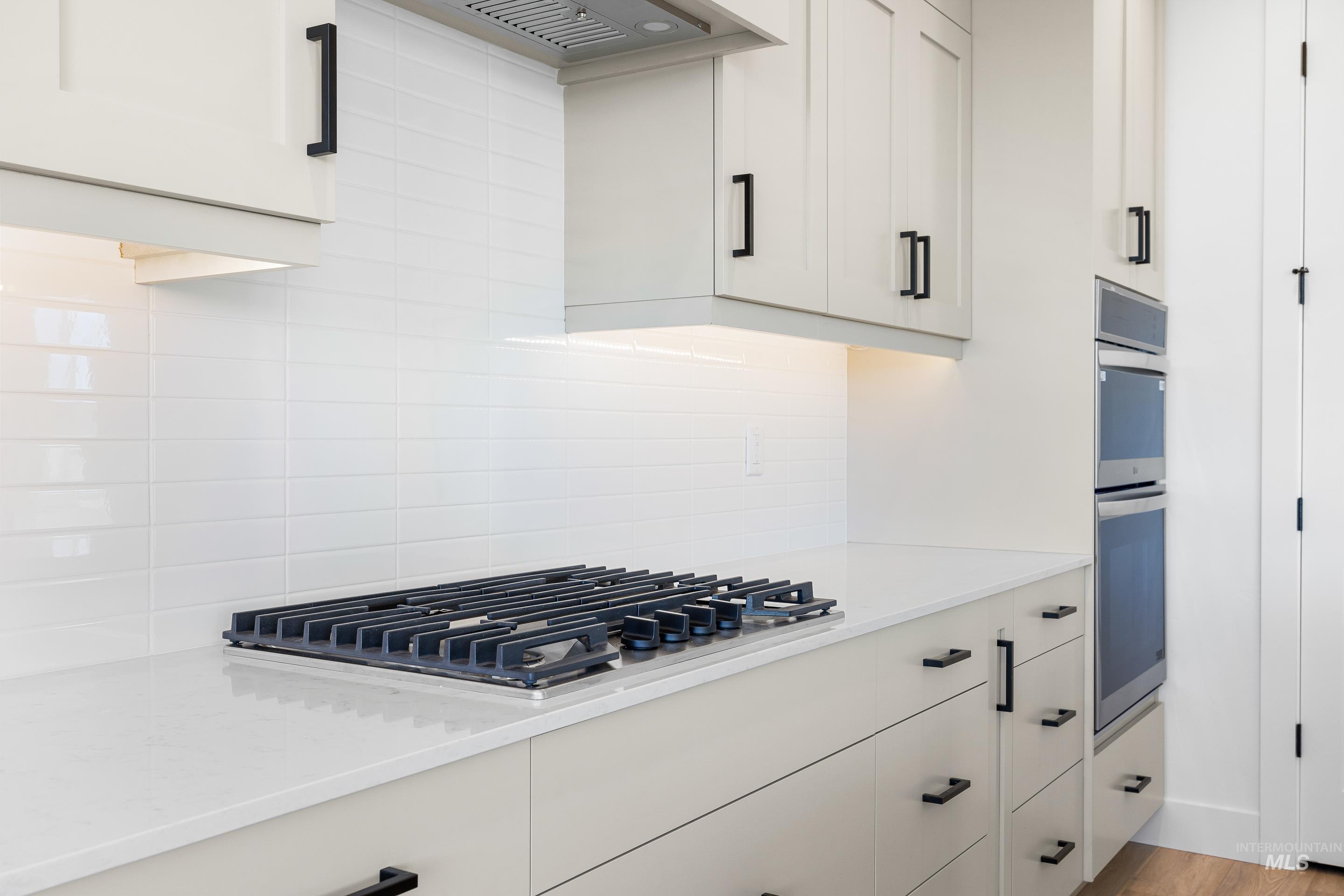 Kitchen featuring light stone countertops, backsplash, appliances with stainless steel finishes, white cabinetry, and premium range hood