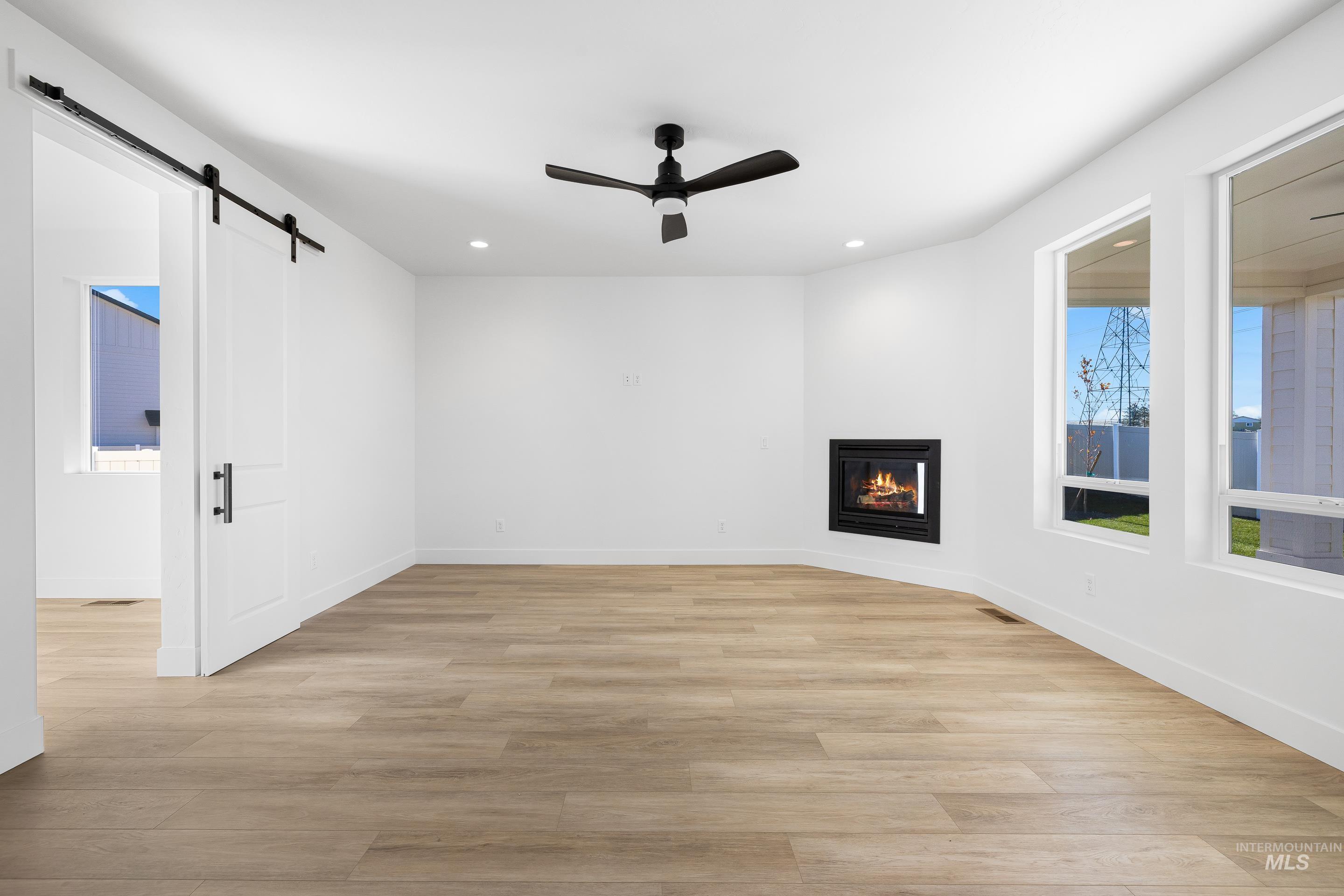 Unfurnished living room featuring a glass covered fireplace, light wood-style floors, a barn door, a ceiling fan, and recessed lighting