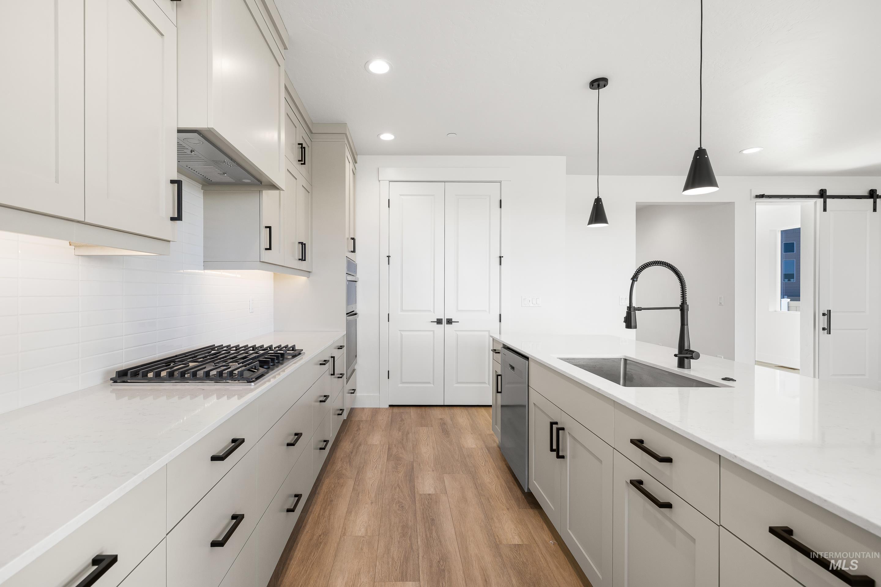 Kitchen with light wood-style flooring, hanging light fixtures, a barn door, light stone counters, and backsplash