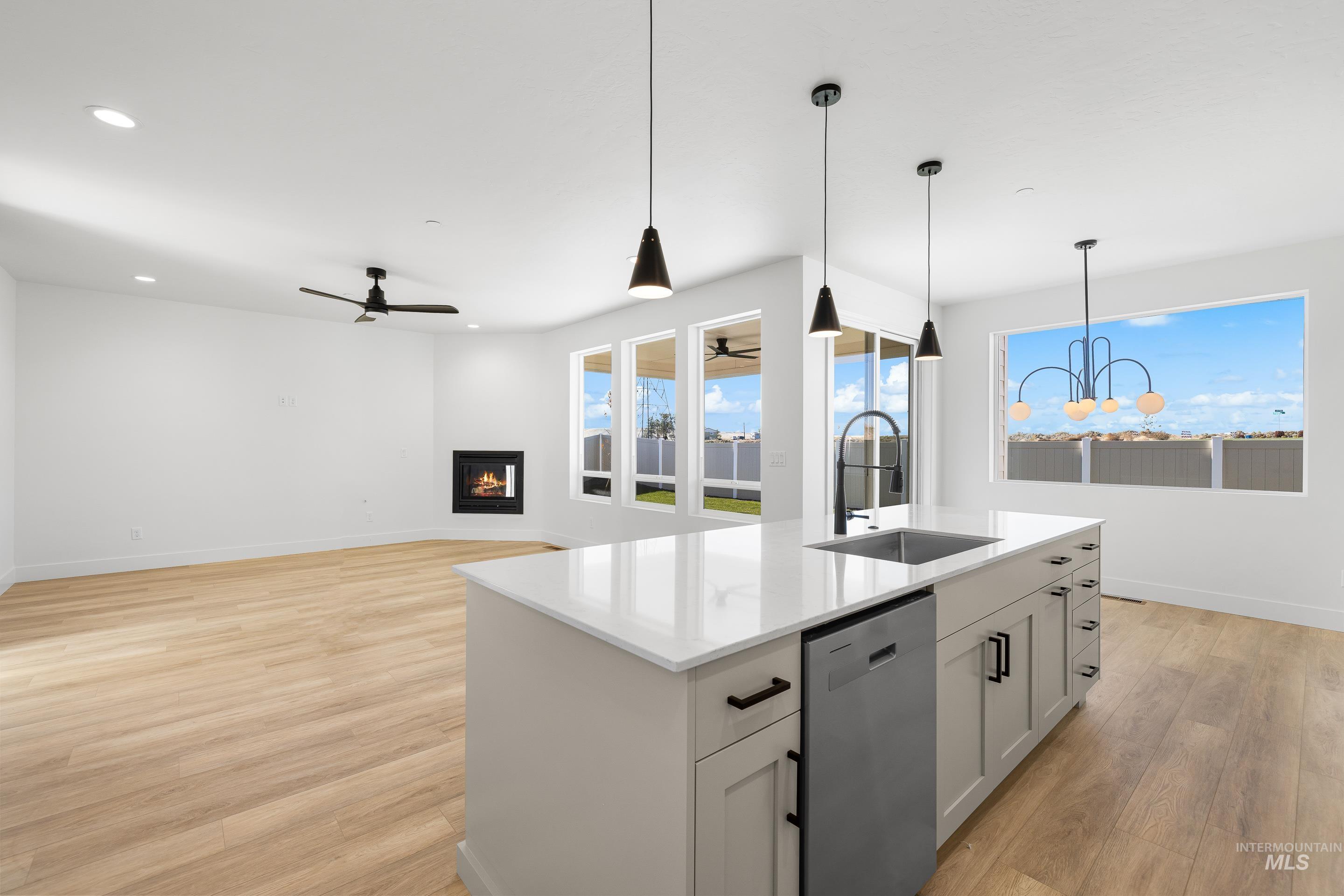 Kitchen featuring decorative light fixtures, stainless steel dishwasher, light wood-style flooring, an island with sink, and a glass covered fireplace