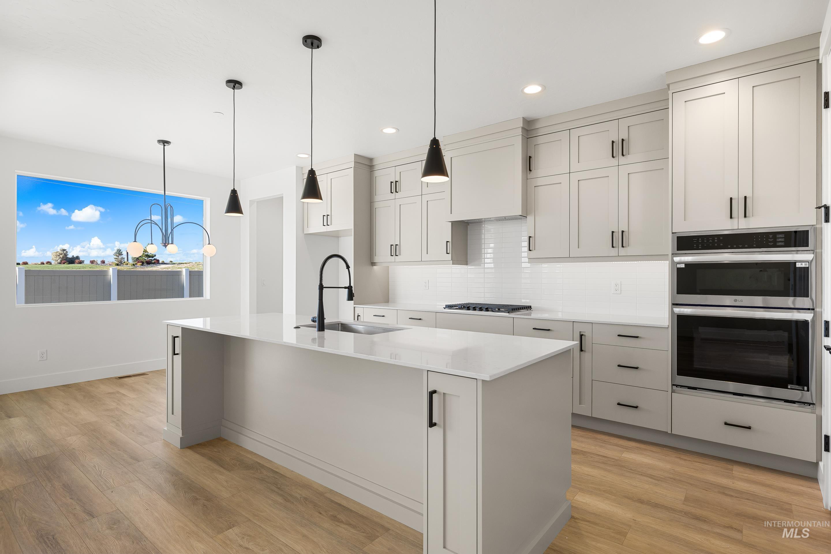 Kitchen with tasteful backsplash, light stone counters, appliances with stainless steel finishes, hanging light fixtures, and recessed lighting