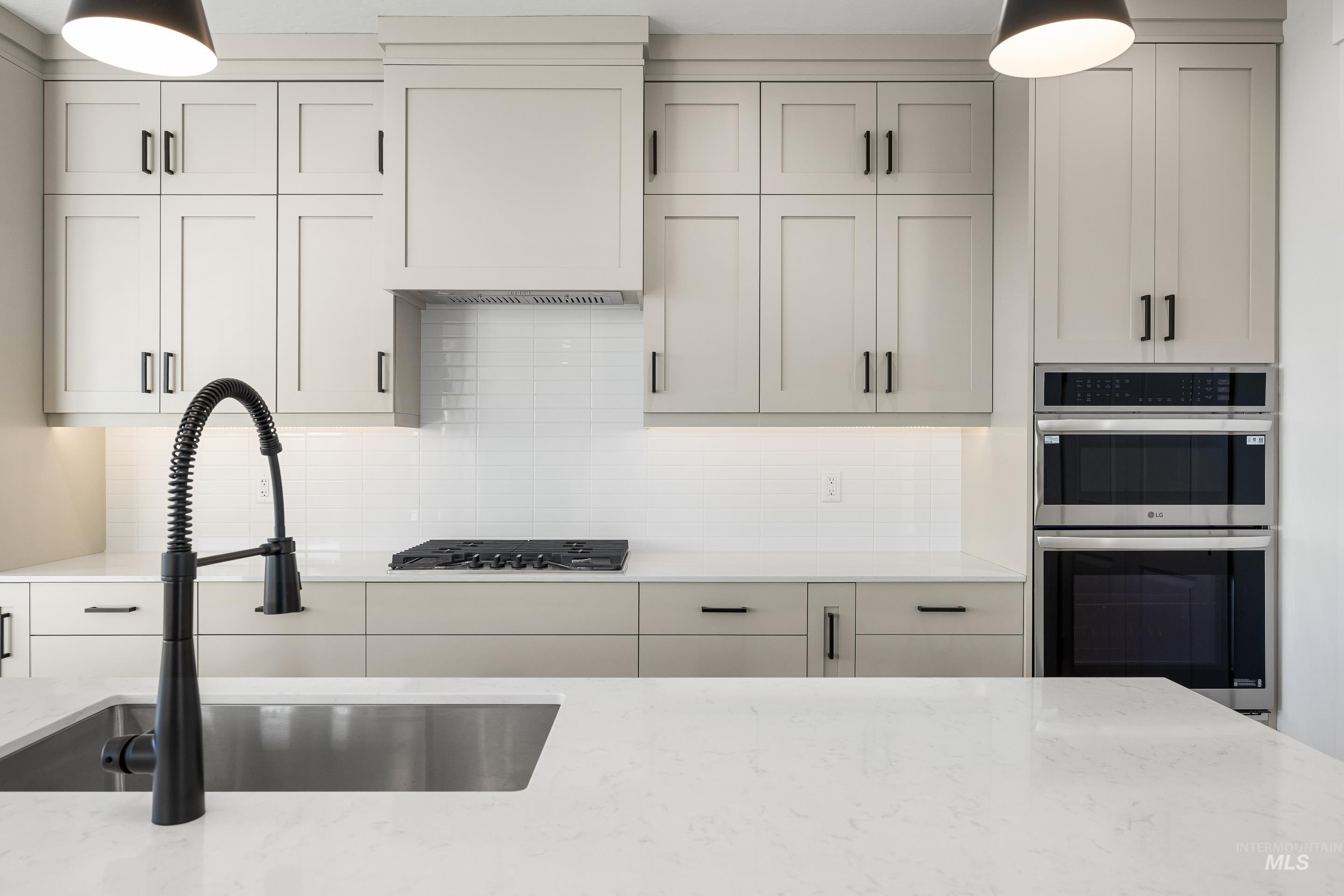 Kitchen featuring hanging light fixtures, light stone counters, stainless steel appliances, and backsplash