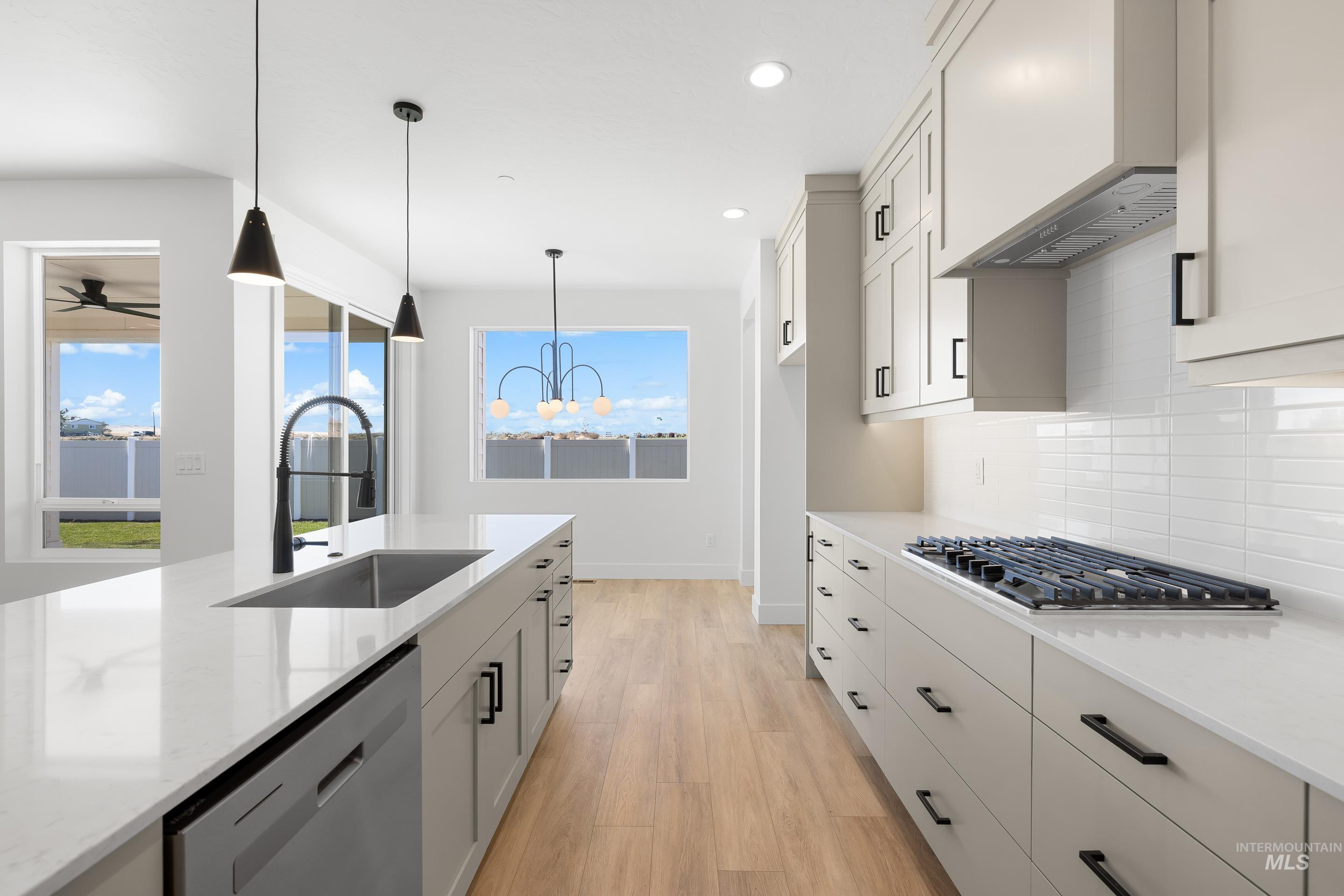 Kitchen featuring light wood-type flooring, light stone counters, stainless steel appliances, pendant lighting, and recessed lighting