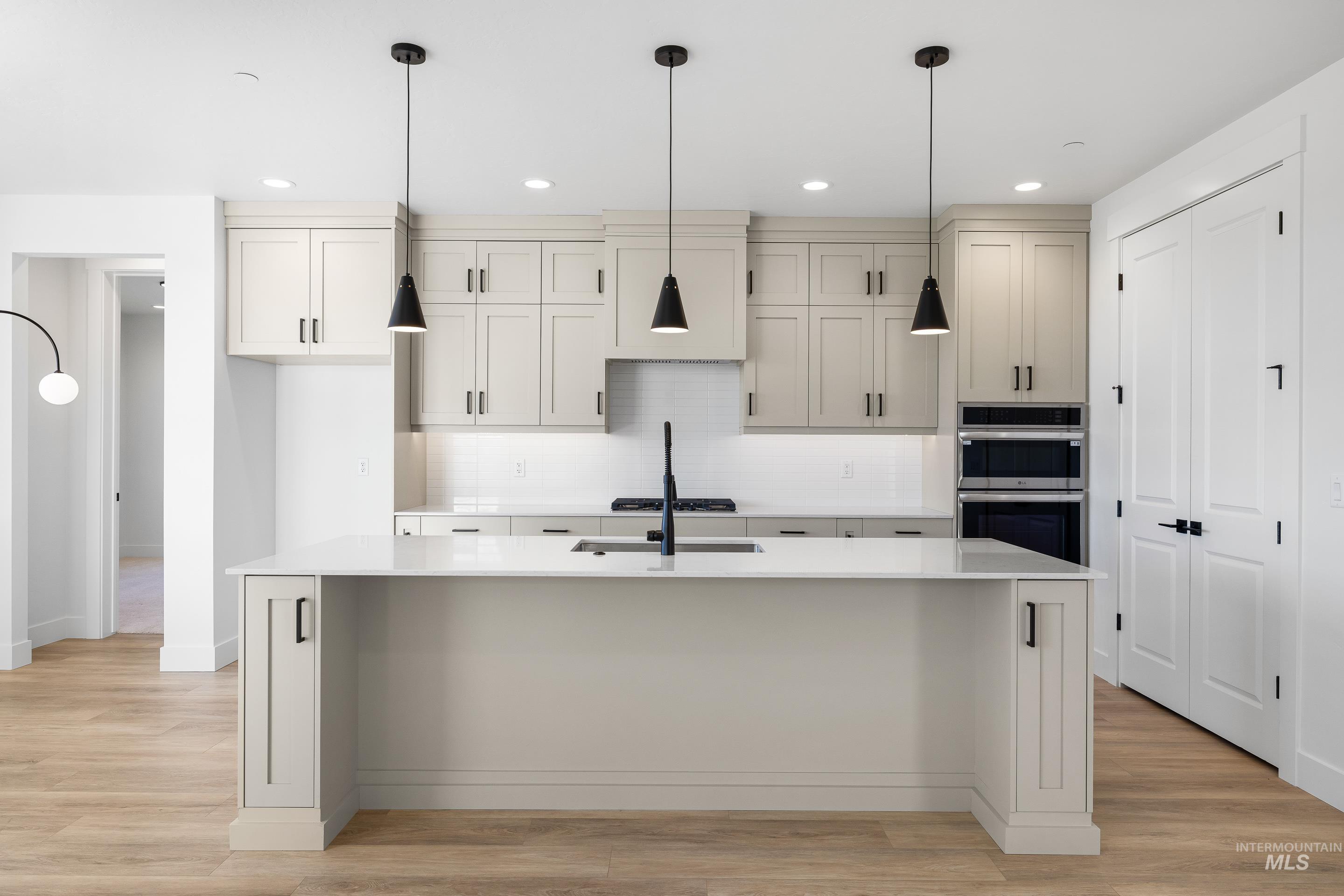 Kitchen featuring pendant lighting, backsplash, light stone countertops, light wood-style flooring, and stainless steel appliances