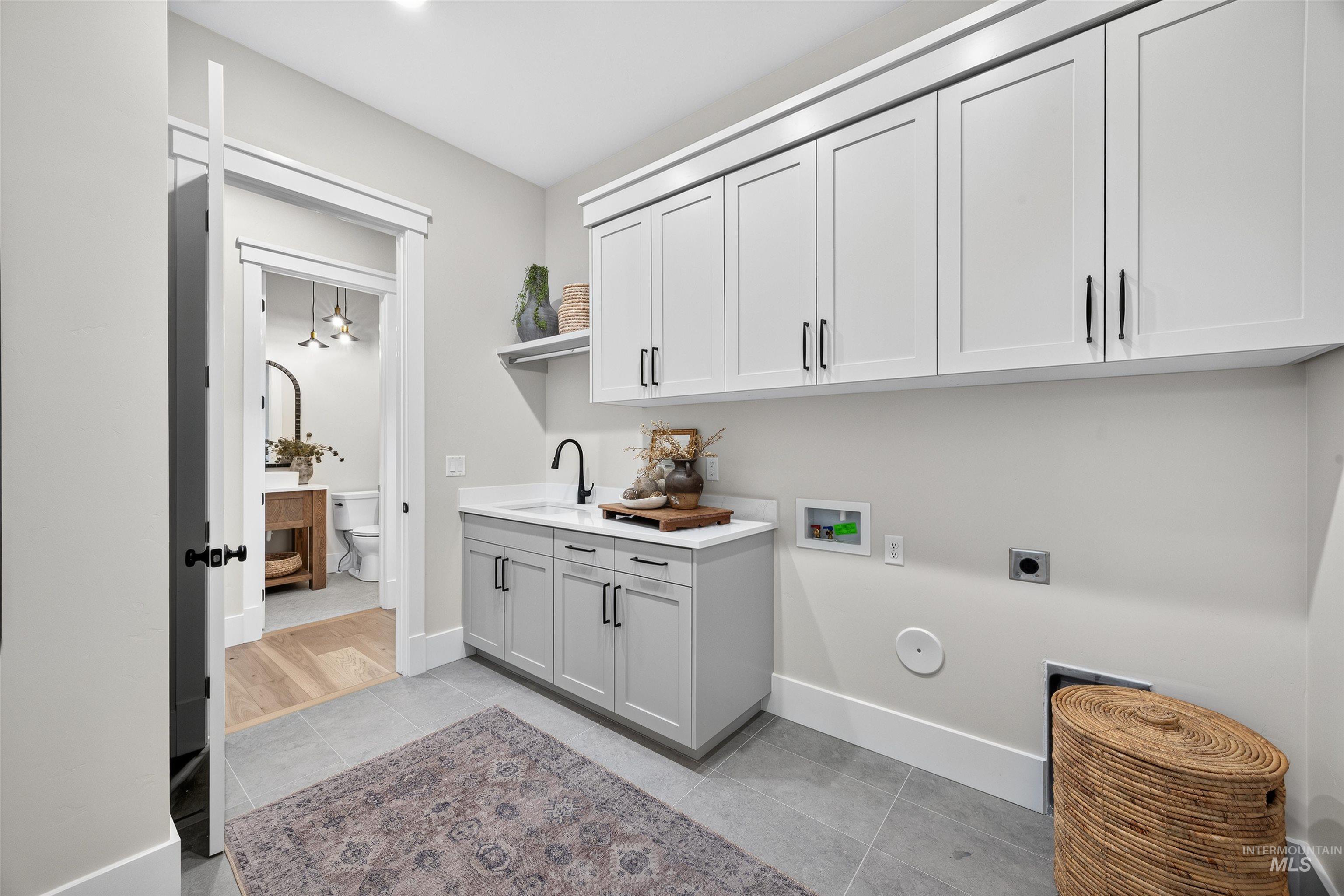 Laundry area featuring upper white cabinetry, lower grey cabinetry, a built-in sink with a black faucet, and light grey floor tiles