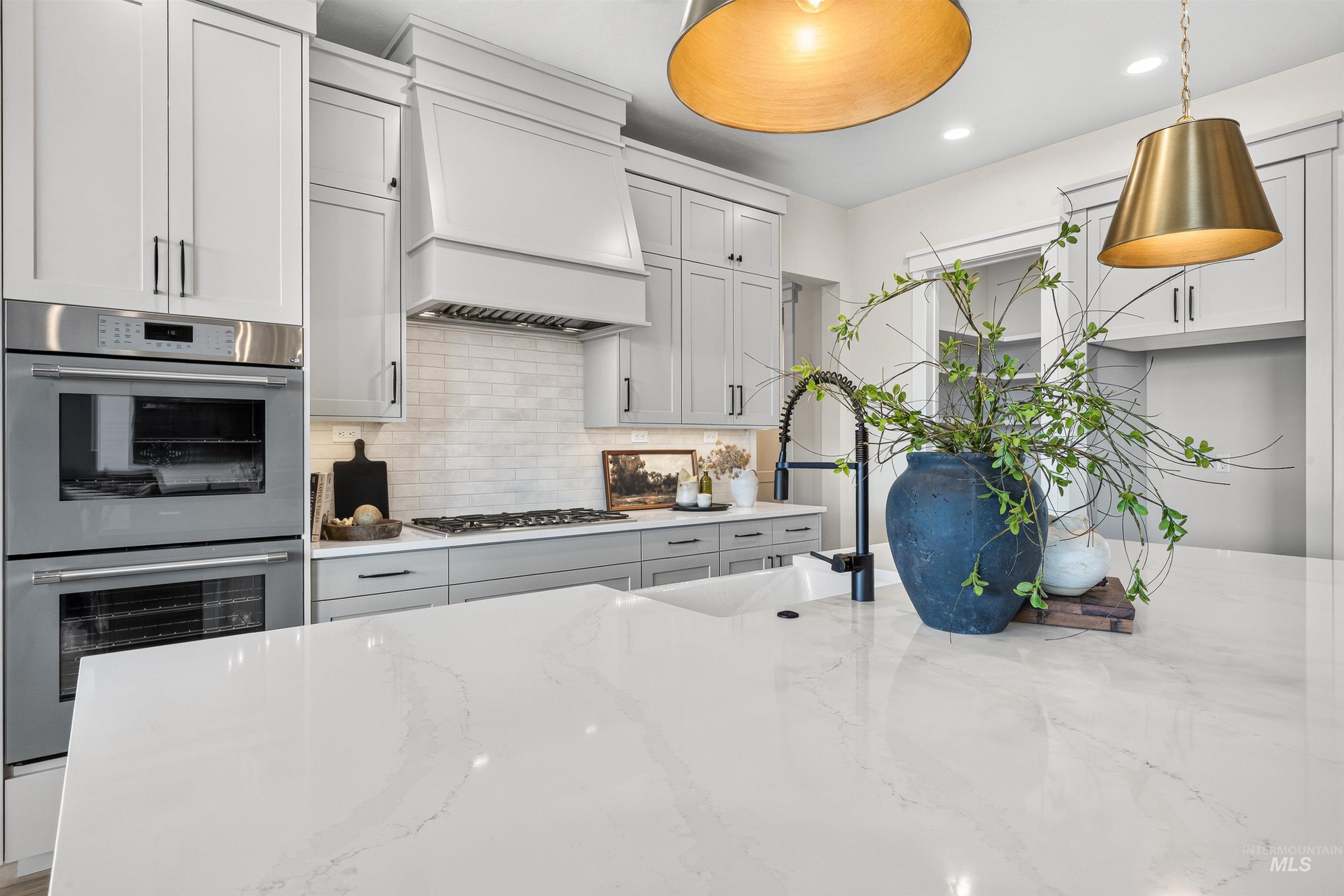 Gourmet kitchen featuring a large island with a gooseneck faucet, light gray cabinetry, stainless steel double ovens, a gas cooktop, and a subway tile backsplash