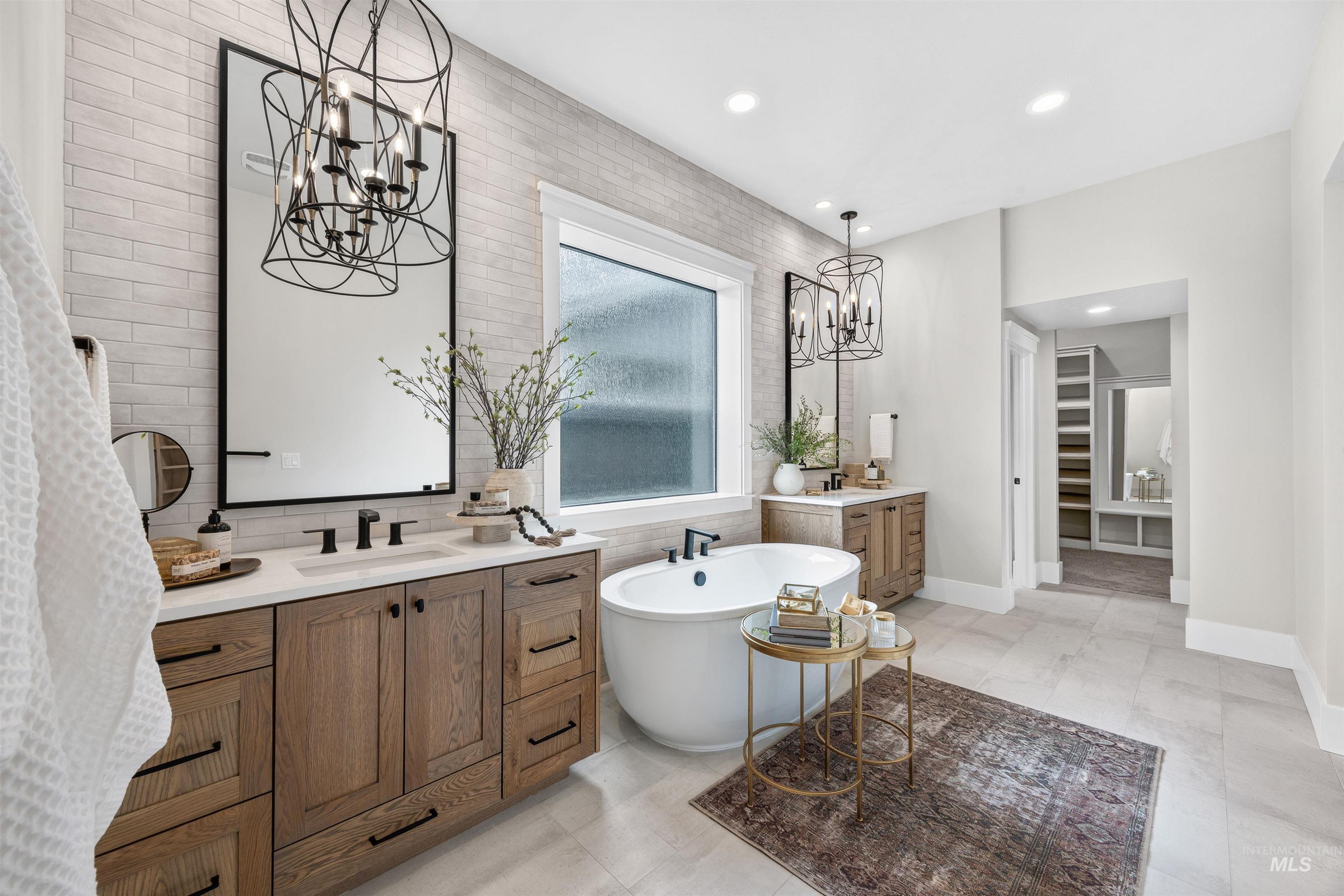 Spacious bathroom featuring a freestanding soaking tub, dual wood-finish vanities with undermount sinks, and a large window with privacy glass