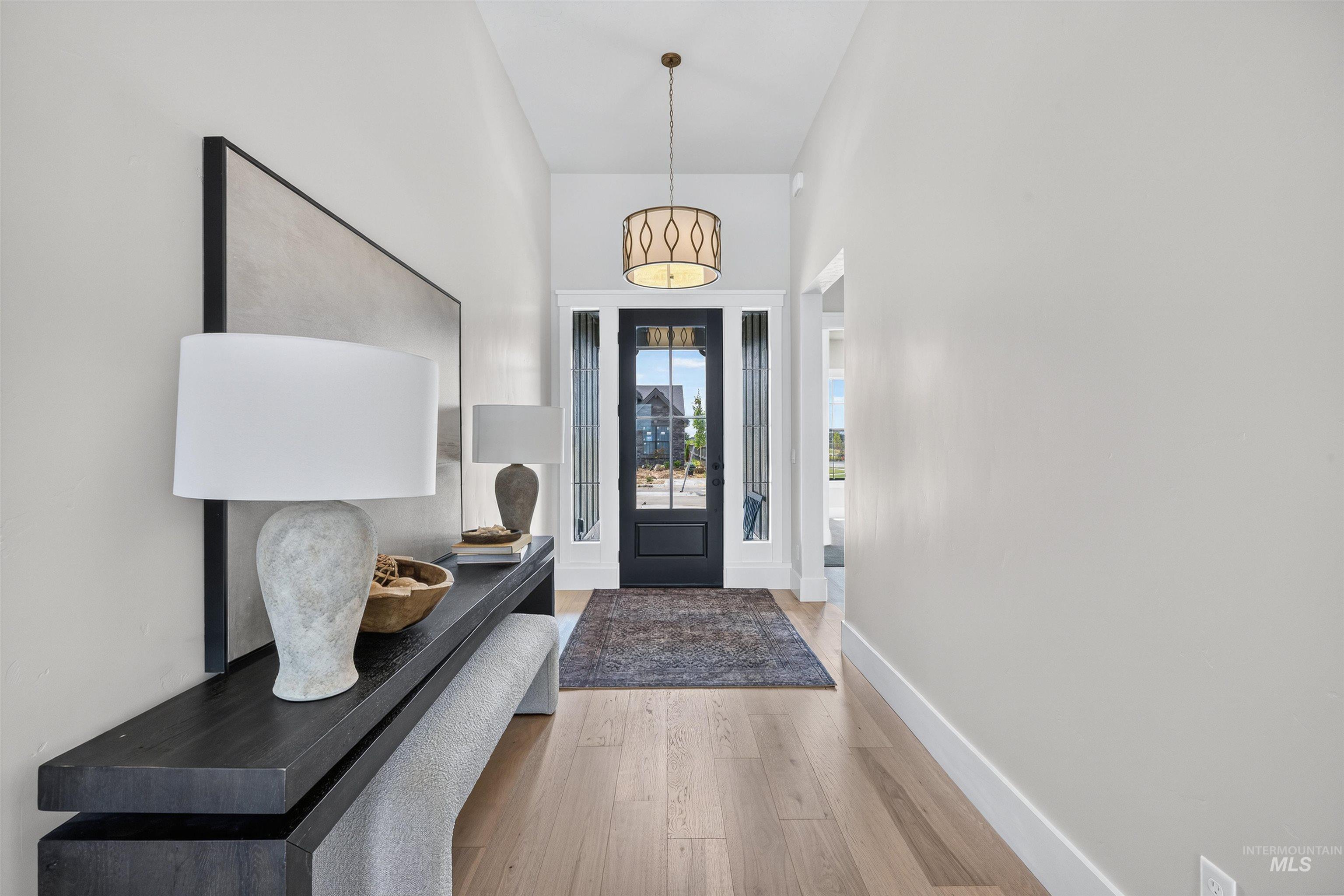 Entryway featuring light wood-finish flooring, a dark paneled door with sidelights, and a decorative overhead pendant light