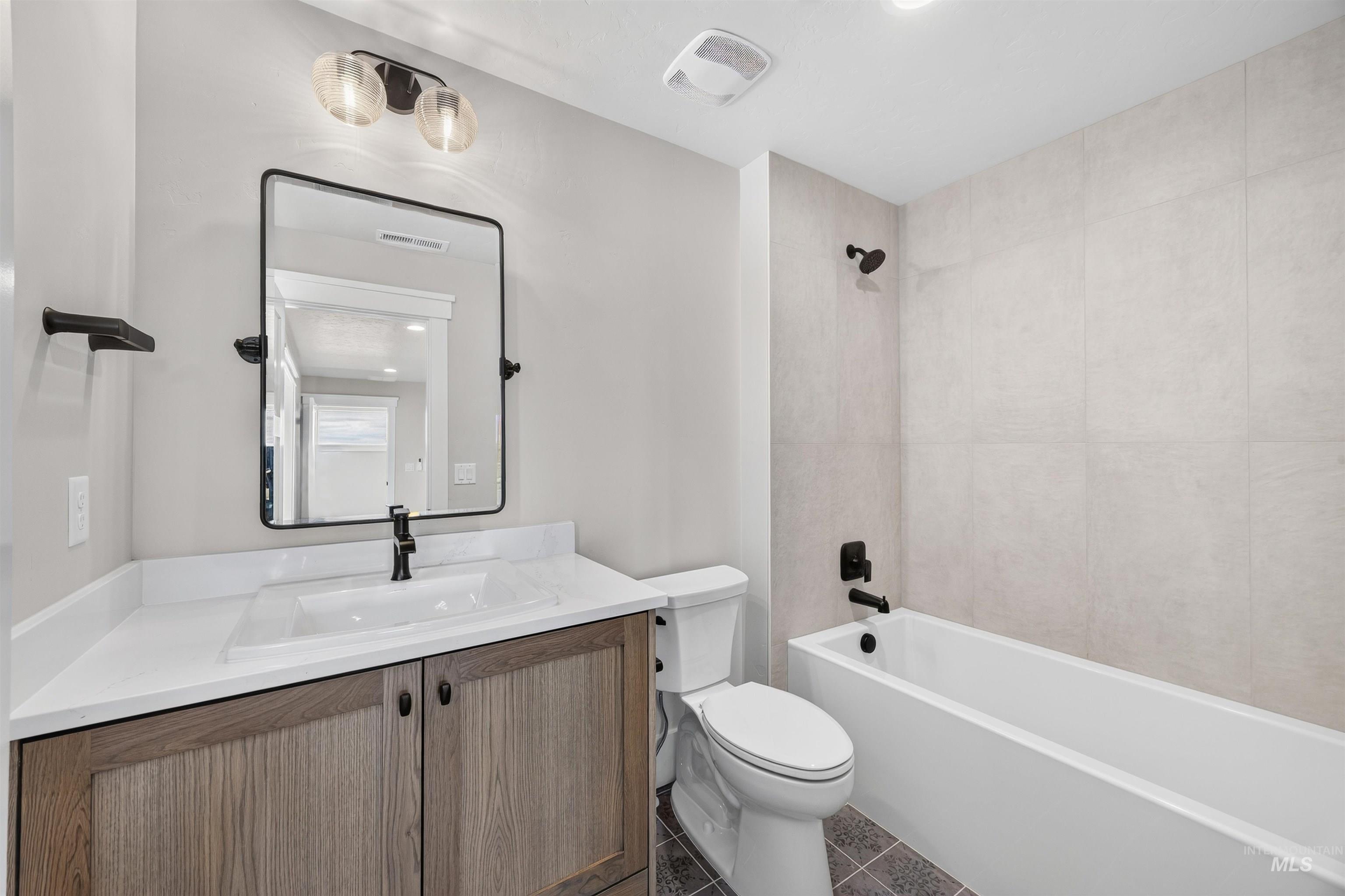 Bathroom featuring a wood-finish vanity with a white countertop and integrated sink, a rectangular framed mirror, and a white bathtub with tile surround