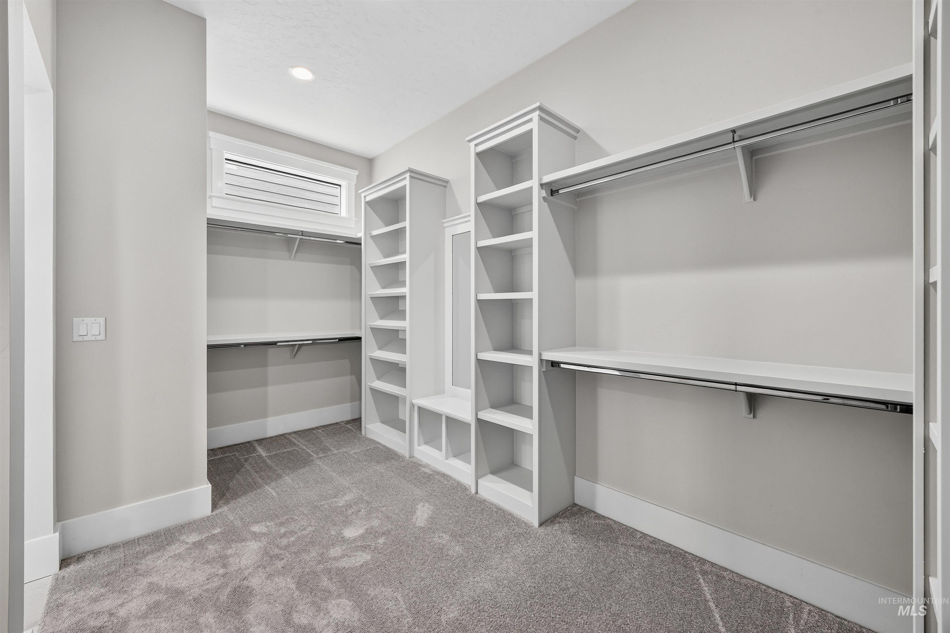 Walk-in closet featuring built-in shelving, hanging rods, an integrated bench, and light gray patterned carpeting