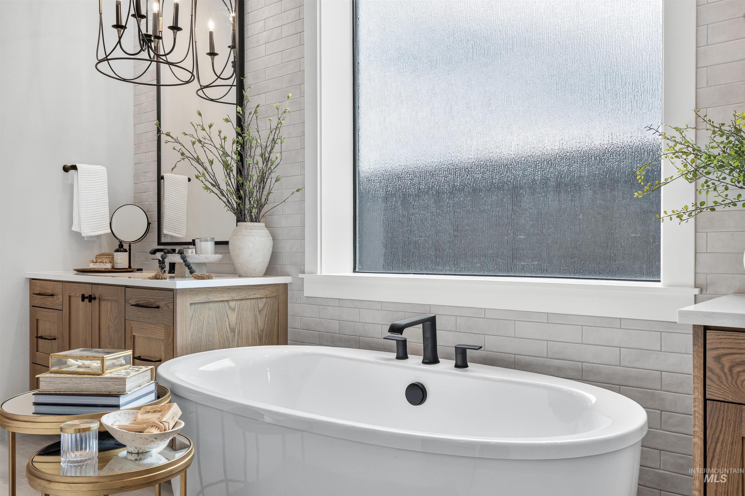 Freestanding soaking tub with matte black fixtures, positioned below a large privacy glass window