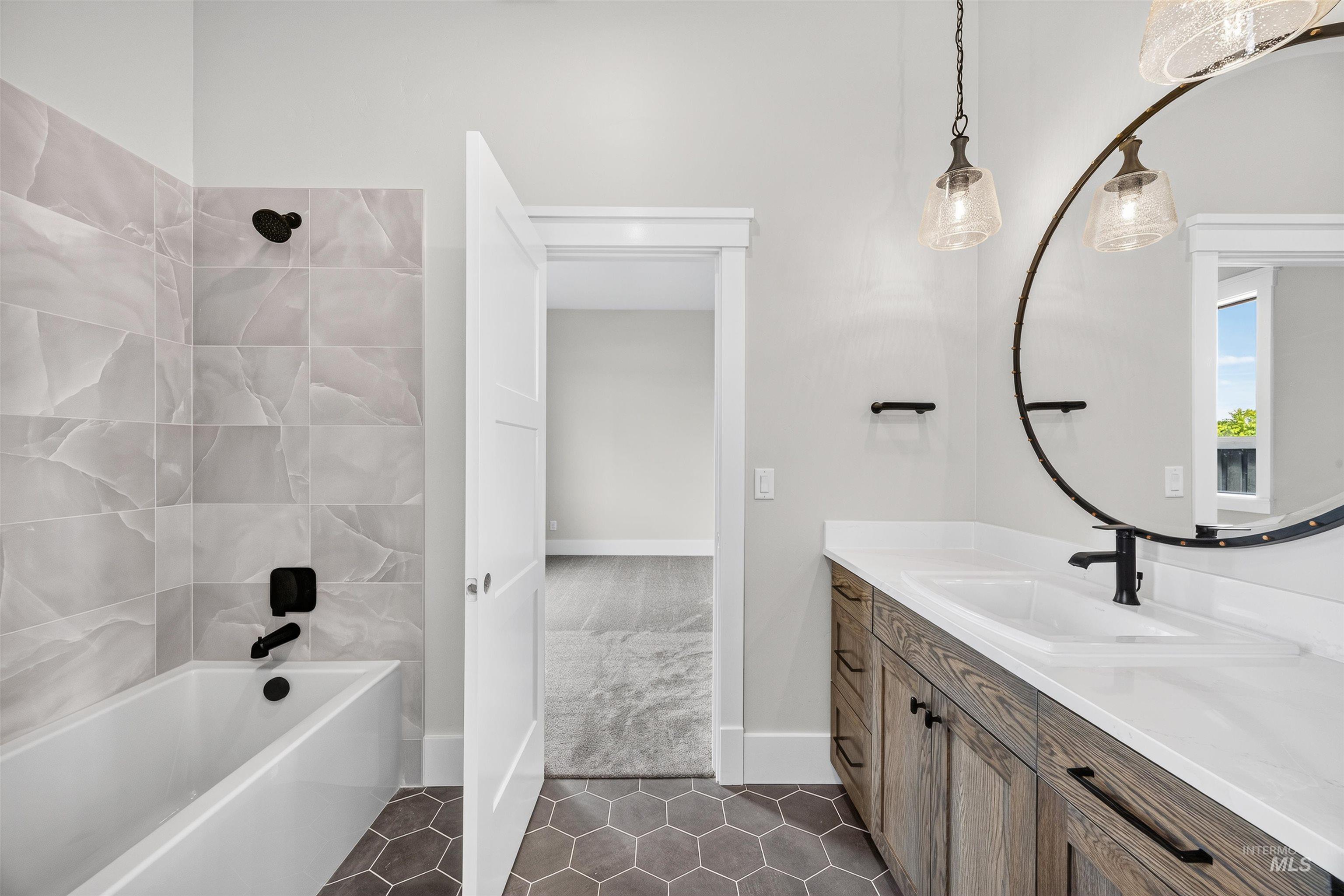 Bathroom featuring a white soaking tub with light-toned tiled surround, a wood-finish vanity with an integrated sink and white countertop, and hexagonal floor tiles