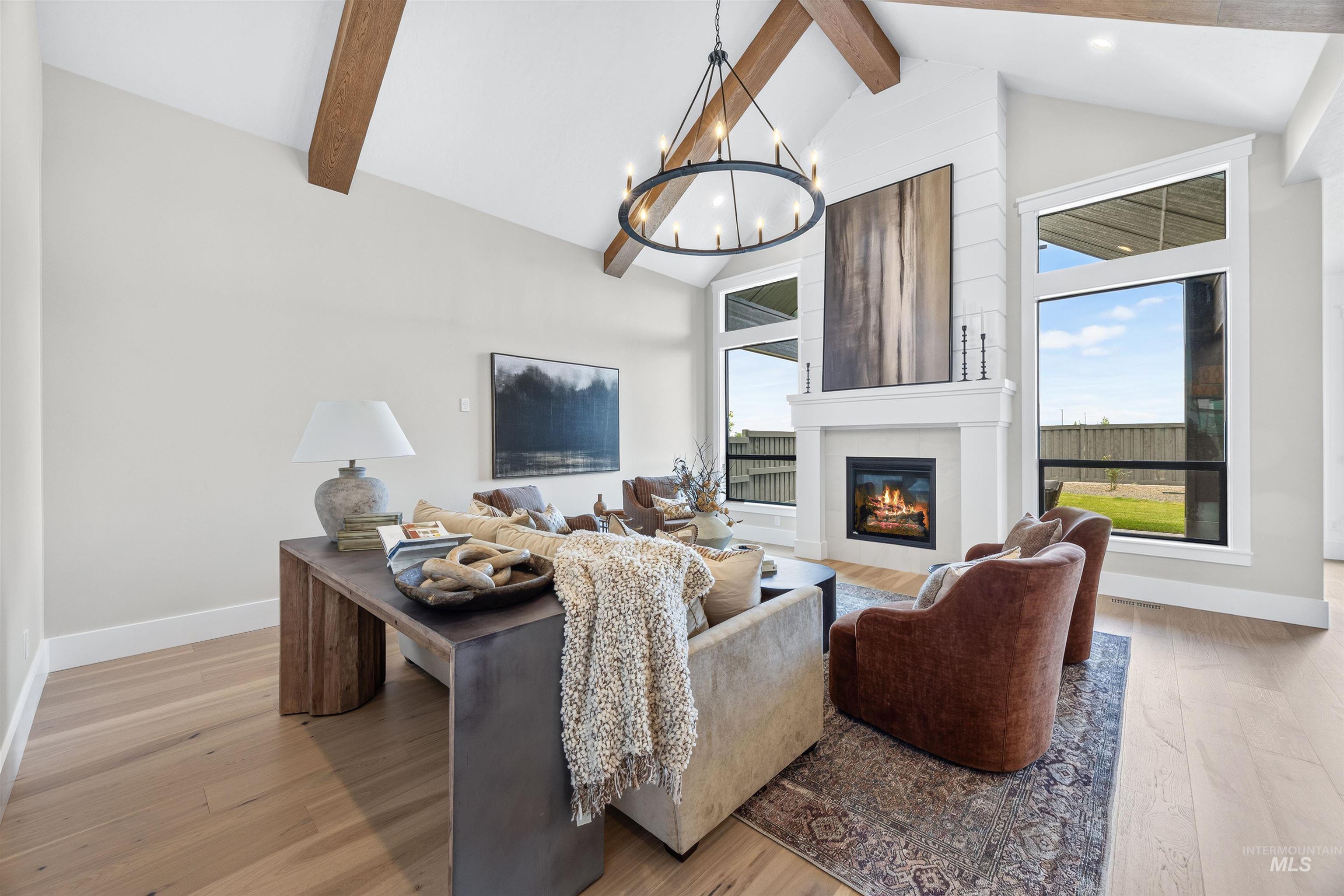 Great room featuring a vaulted ceiling with exposed wood beams, a central chandelier, and light wood-finish flooring