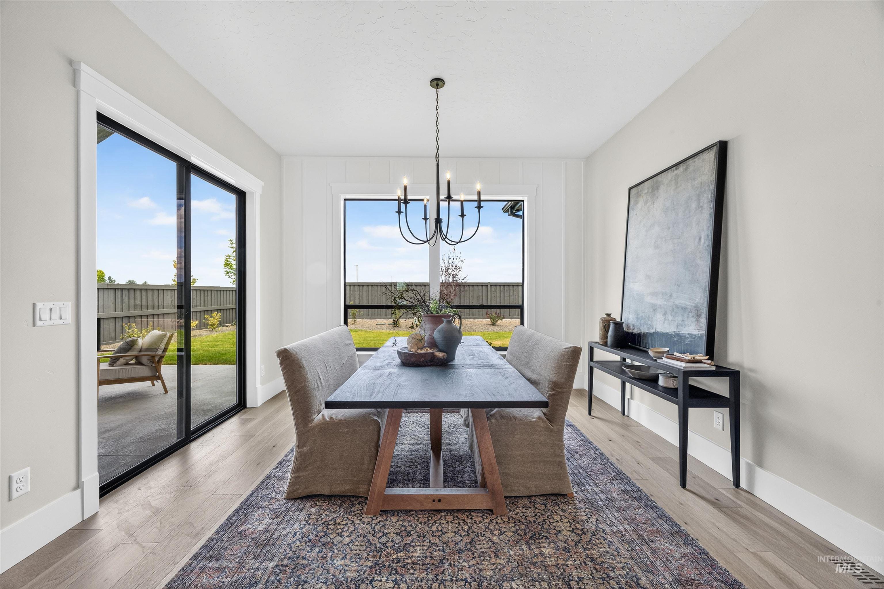 Dining area with light wood-finish flooring, a contemporary chandelier, large picture window, and direct access to the outdoor patio via a sliding glass door