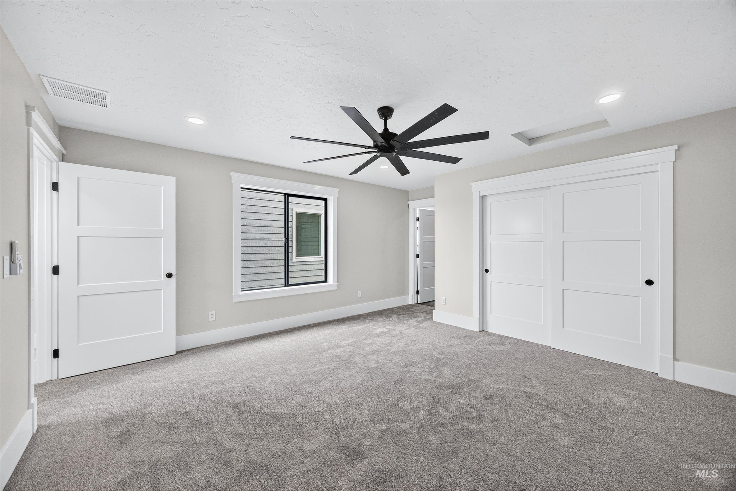Spacious room featuring neutral-toned carpet flooring, a contemporary black ceiling fan, and recessed lighting