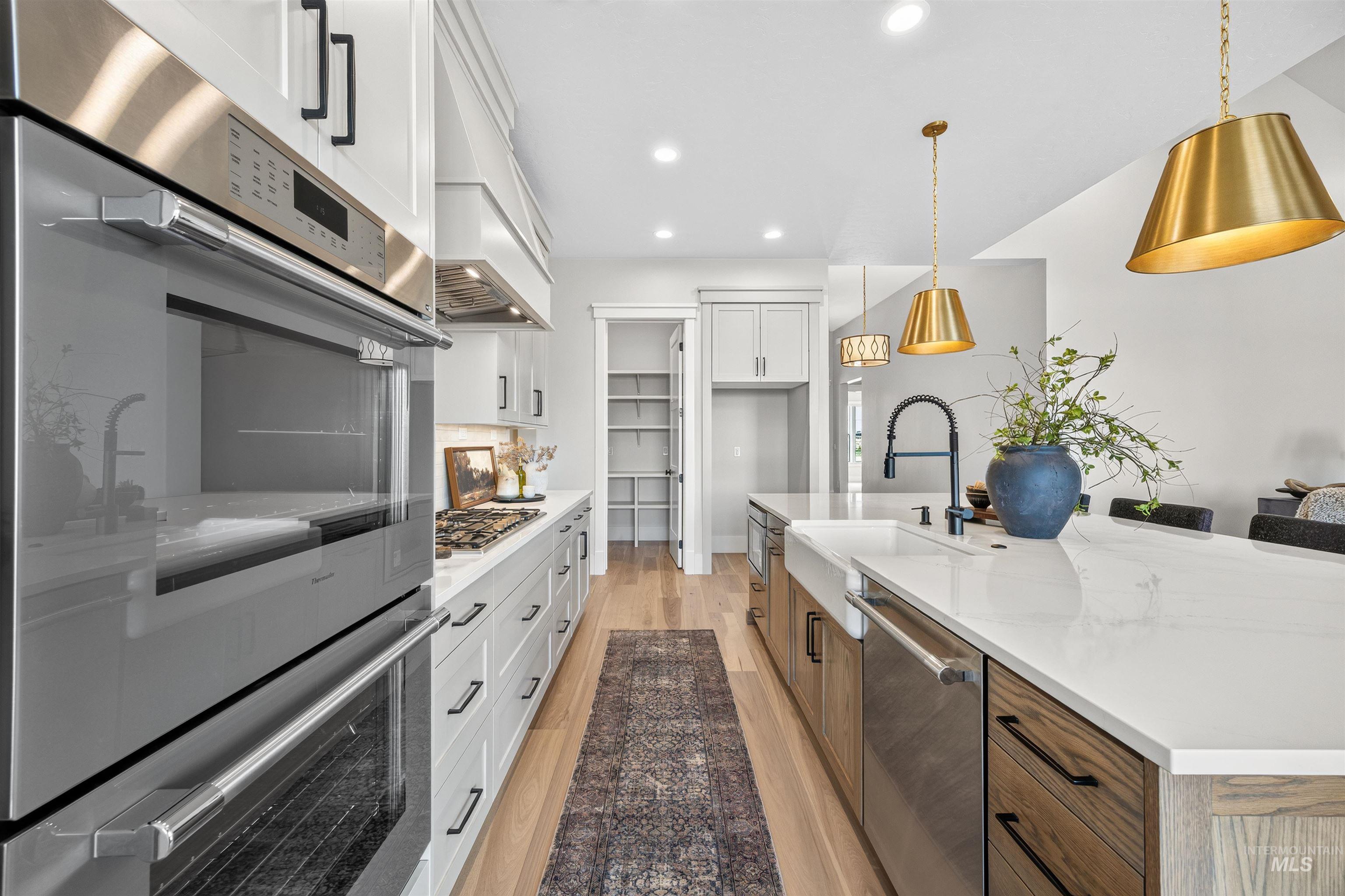Modern kitchen featuring stainless steel double ovens, a gas range, and a large center island with a farmhouse sink