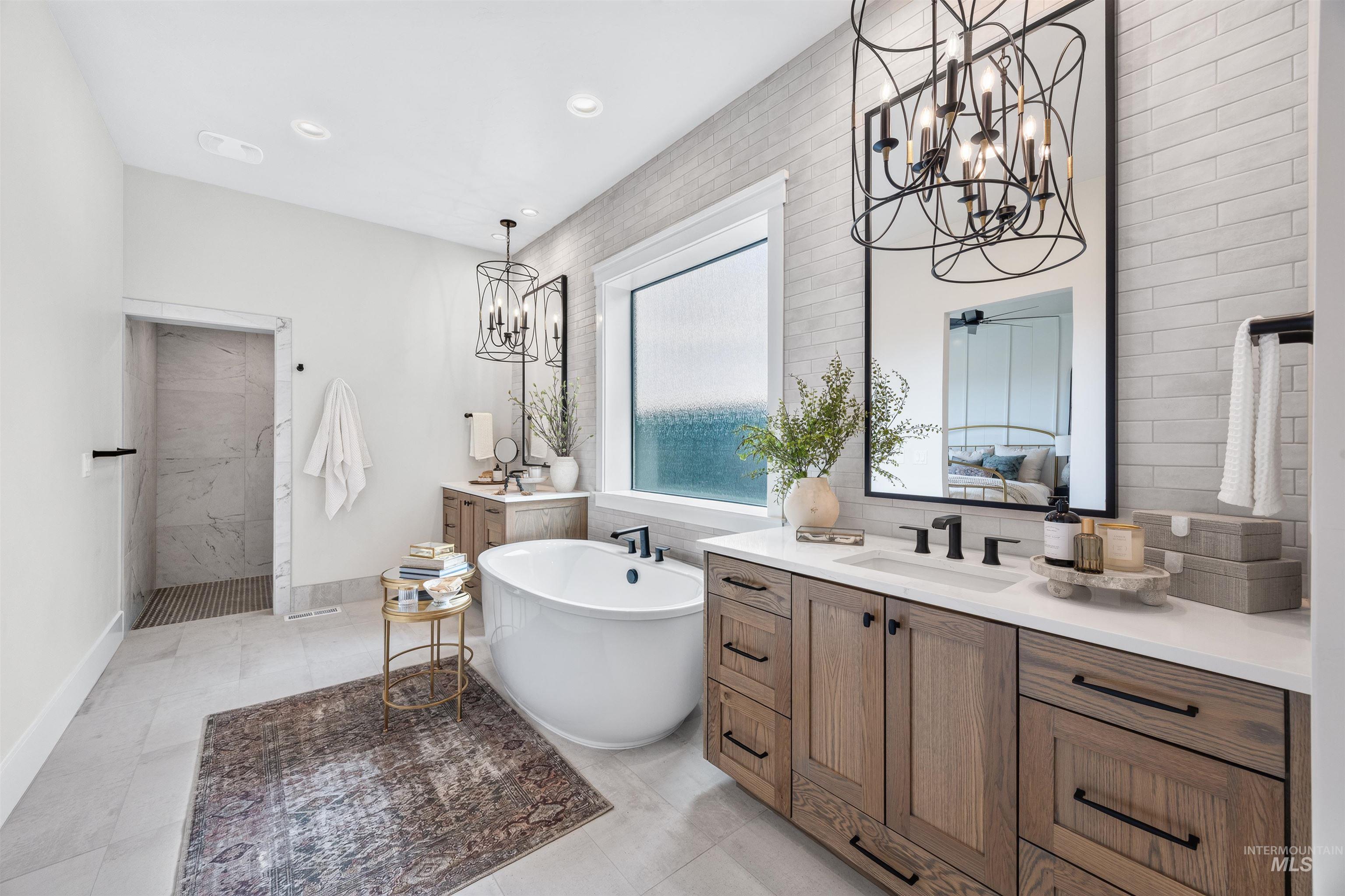 Spacious bathroom featuring a freestanding soaking tub, a walk-in shower with marble-look wall tile, dual wood-finish vanities with white countertops, and contemporary black-framed mirrors with coordinating chandeliers