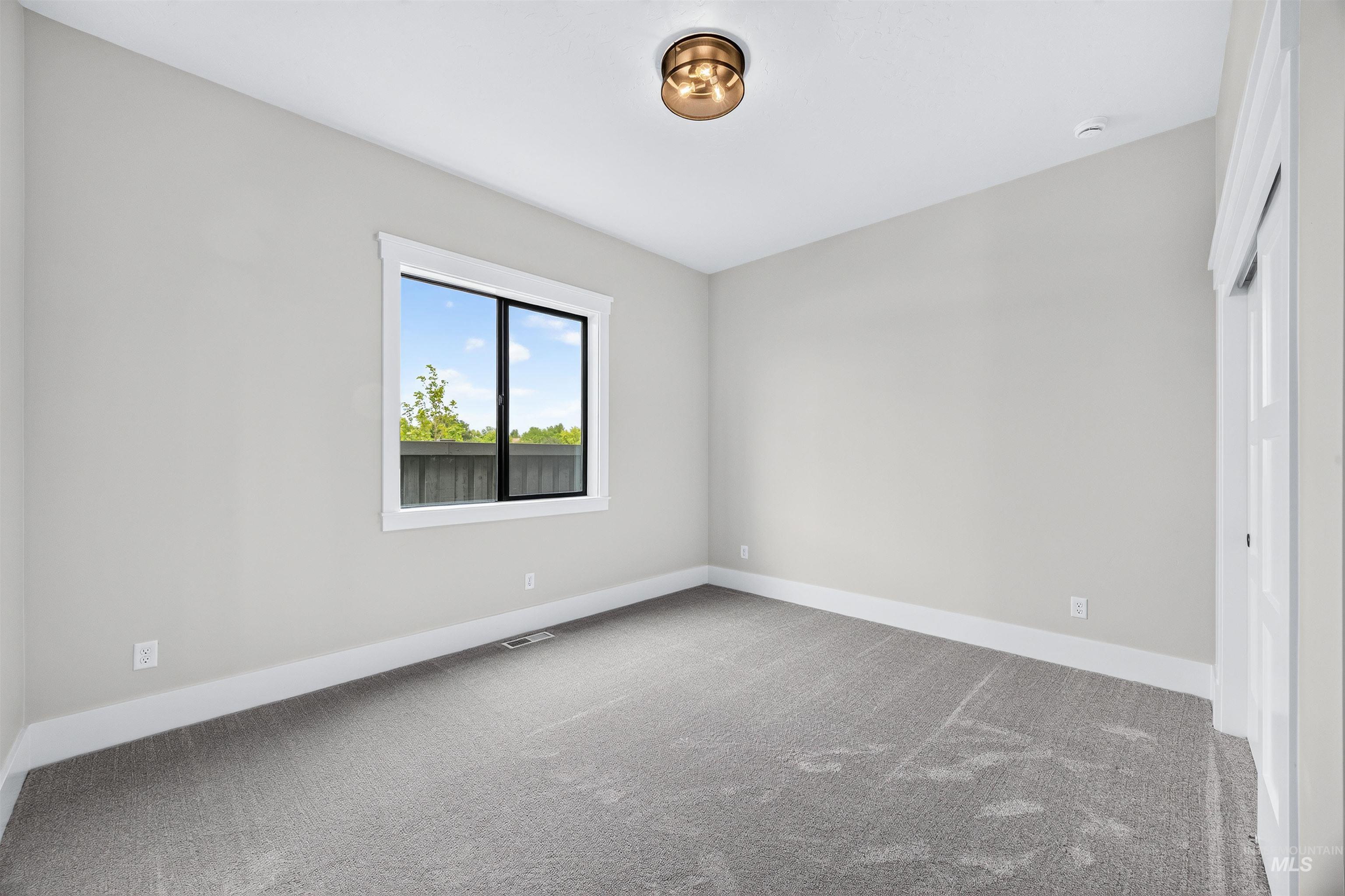 Spacious room featuring neutral carpeting, light gray walls, a contemporary window with white trim, a modern ceiling light fixture, and a paneled door