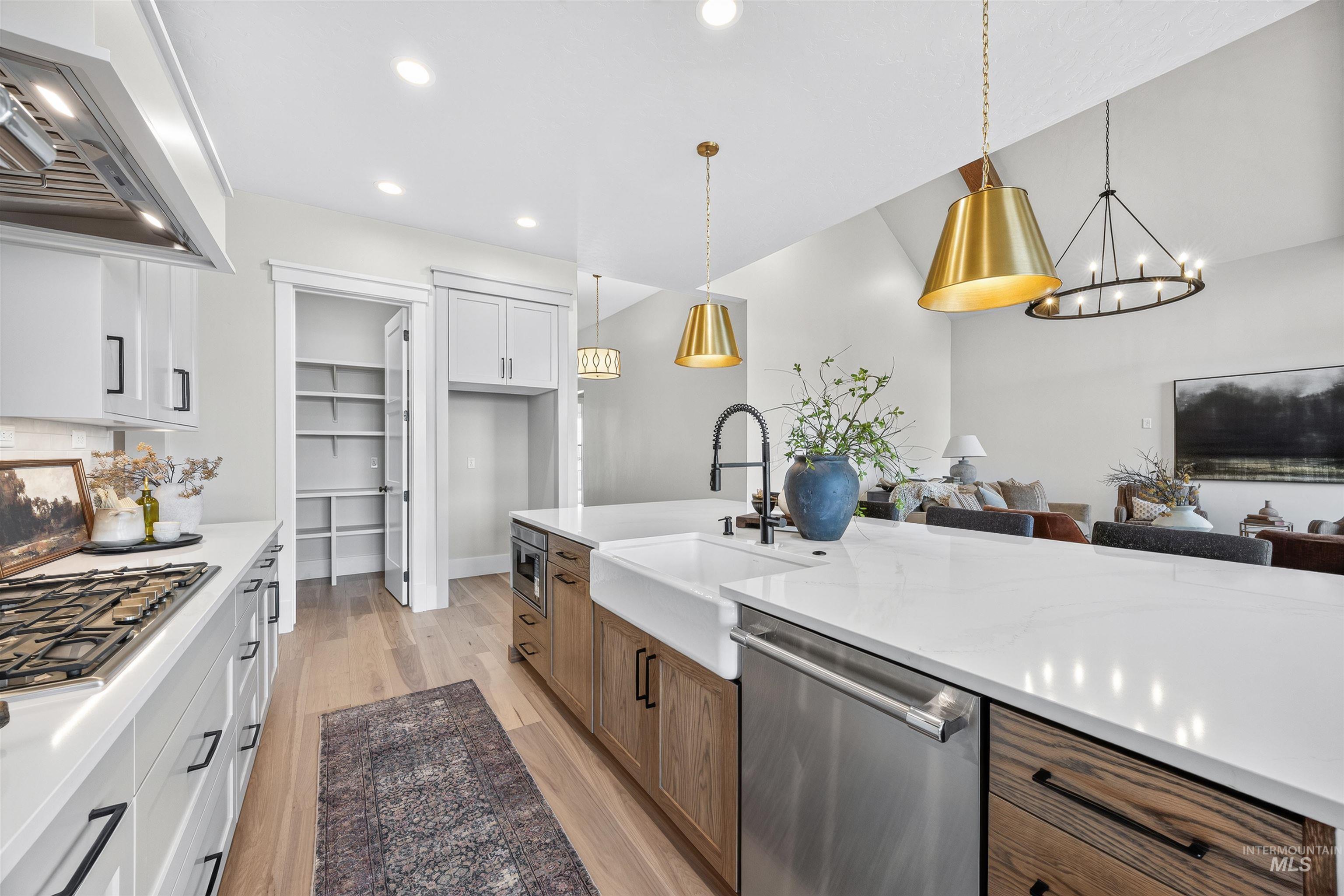 Spacious kitchen featuring a large central island with a farmhouse sink, stainless steel appliances, white cabinetry, wood-finish flooring, and a walk-in pantry