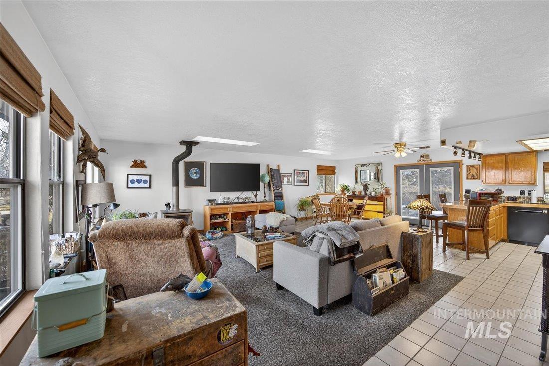Living room featuring a wood stove, a textured ceiling, light tile patterned flooring, and ceiling fan