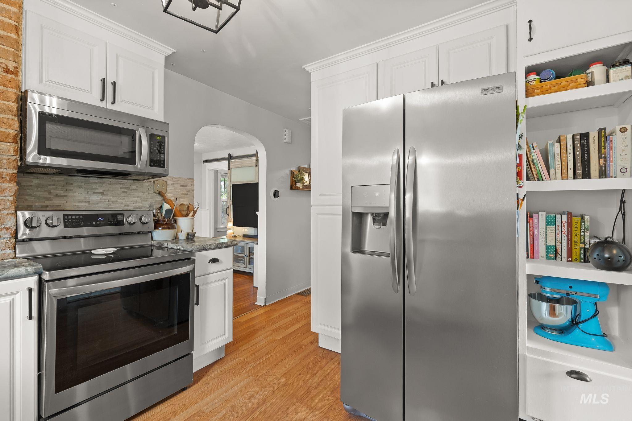 Kitchen featuring stainless steel appliances, white cabinetry, granite countertops, and wood-finish flooring