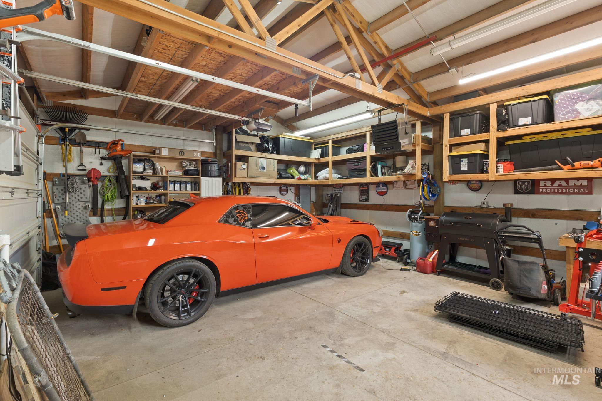 Spacious garage featuring exposed wood beam ceiling, ample built-in shelving, durable concrete flooring, and bright overhead lighting