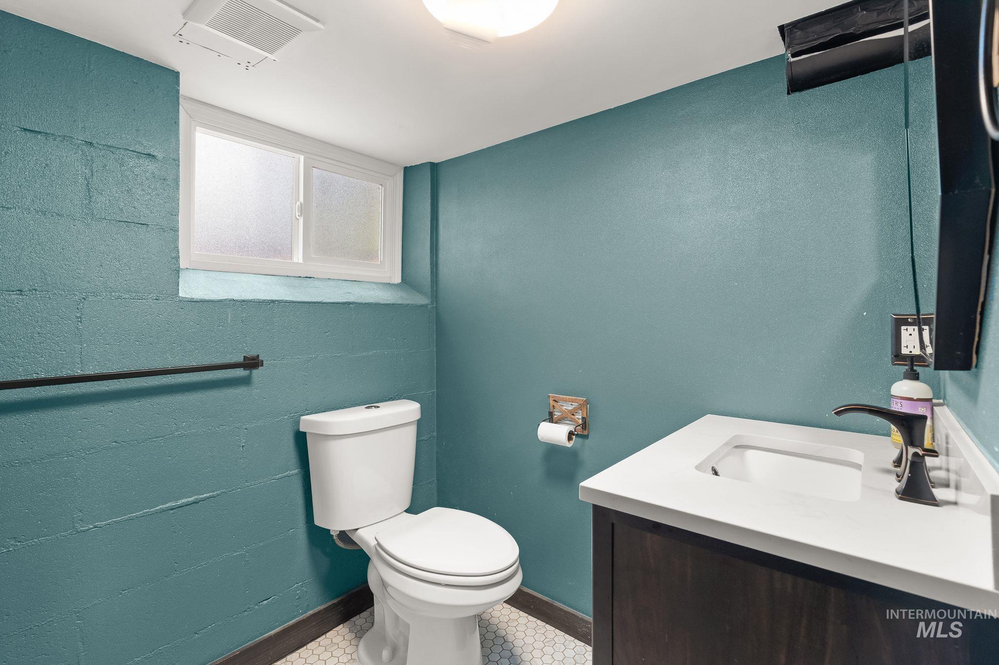 Bathroom featuring a window, white hexagonal floor tiles, a dark wood-finish vanity with a white countertop and integrated sink, a dark bronze-finish faucet, and a wall-mounted toilet