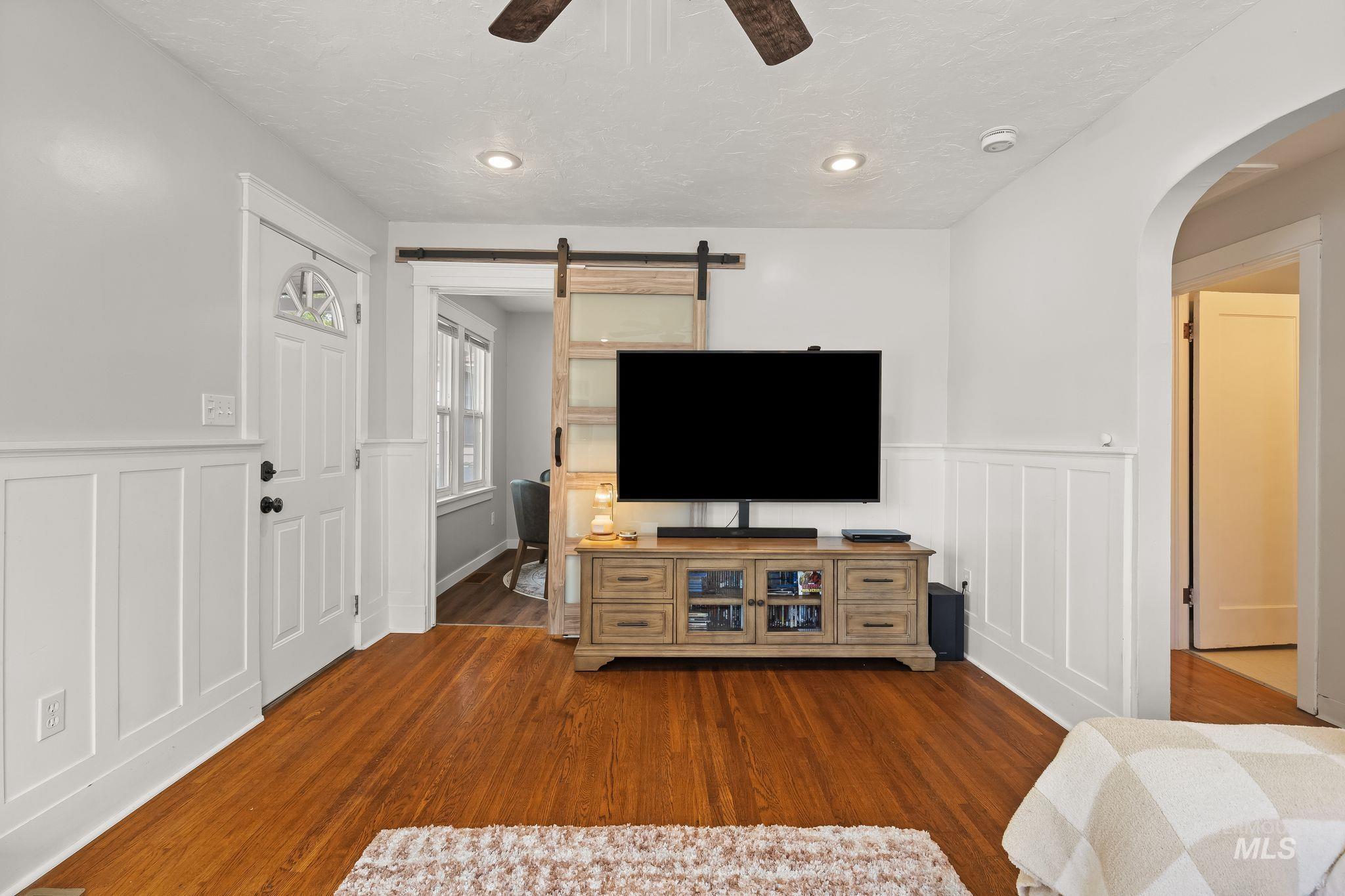 Living area featuring wood-finish flooring, white wainscoting, recessed lighting, and a barn door leading to an additional space