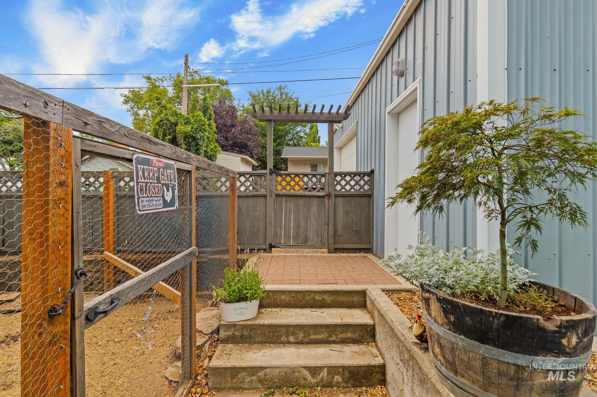 Exterior featuring a light blue corrugated metal facade, a concrete stairwell, a brick paver landing, a wooden privacy fence, and a wooden pergola