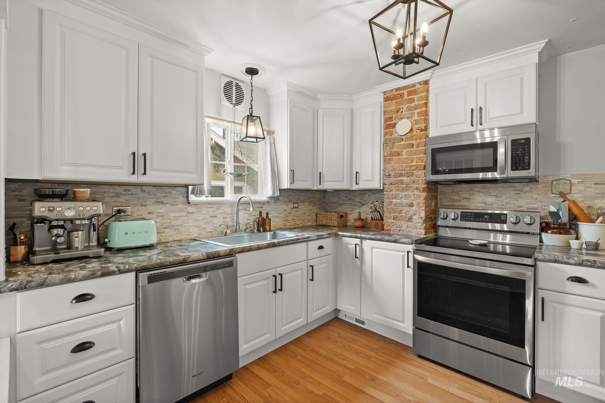 Kitchen featuring white shaker-style cabinetry, stainless steel appliances, dark countertops, a mosaic tile backsplash, and wood-finish flooring