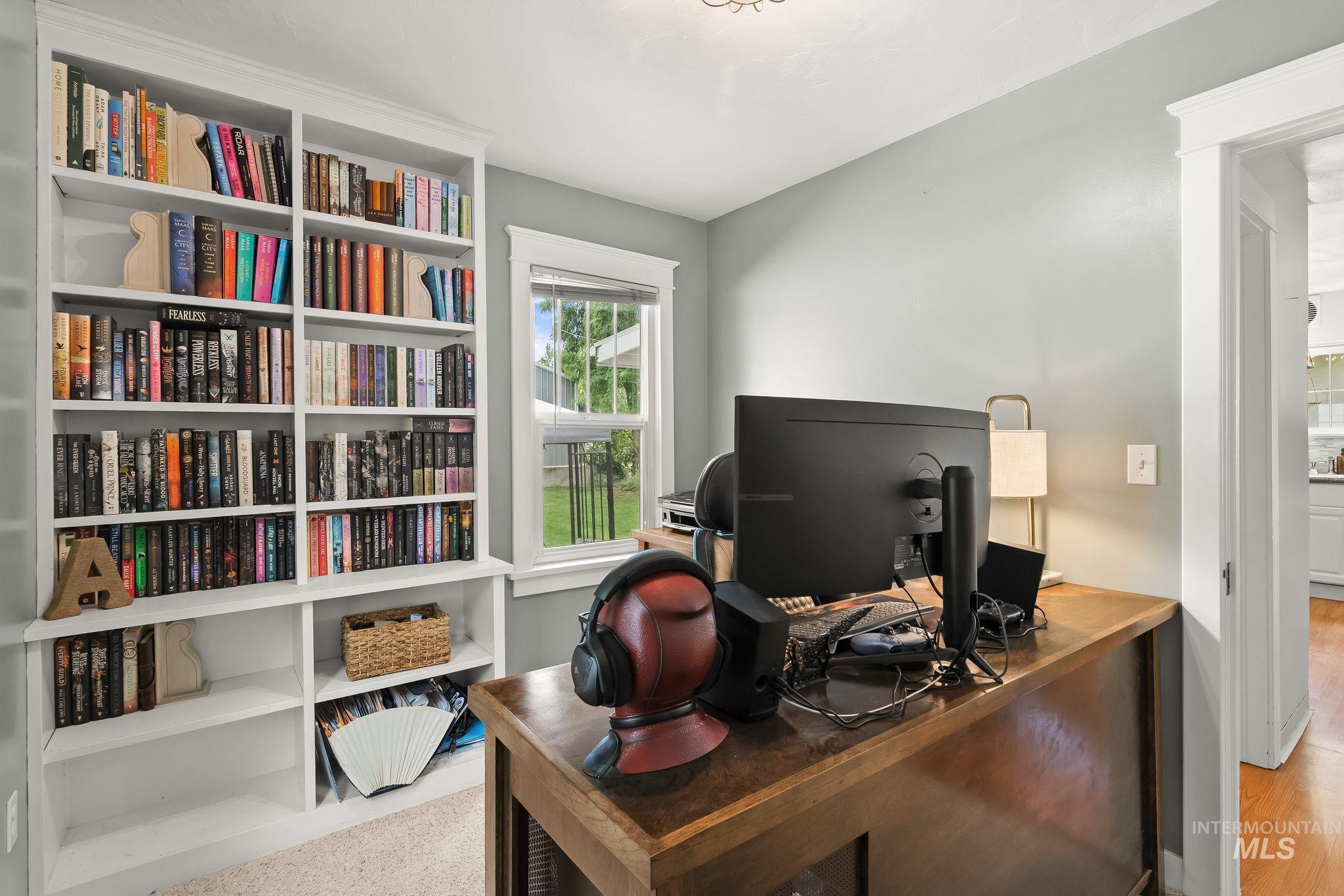 Room with light gray walls featuring a white built-in bookcase, a window with white trim, and a wood-finish desk