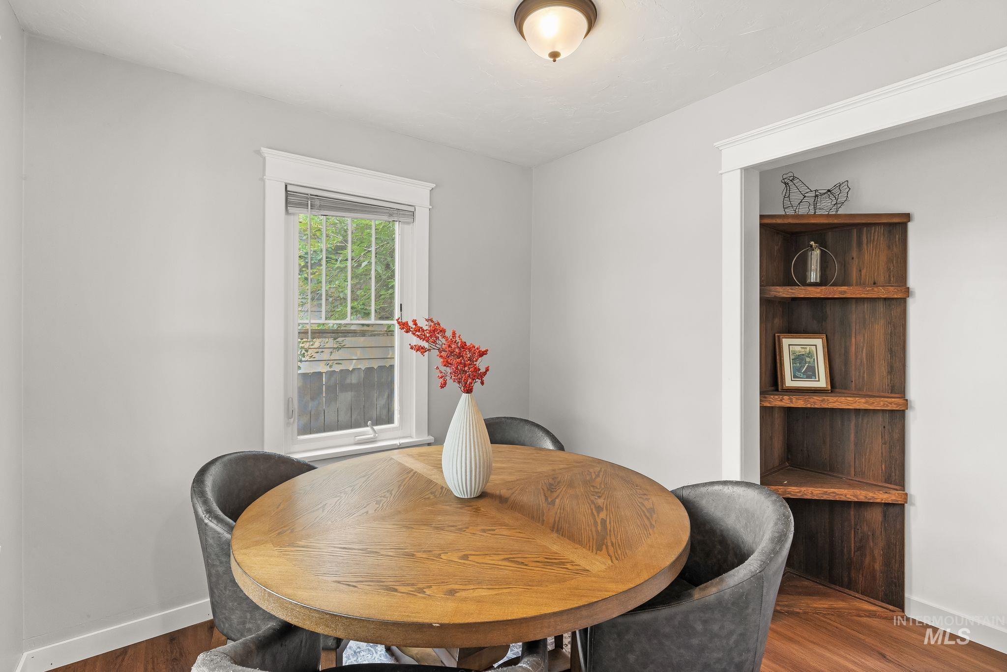 Dining area featuring wood-finish flooring, a built-in corner shelving unit, a window with exterior grilles, and a flush-mount ceiling light fixture