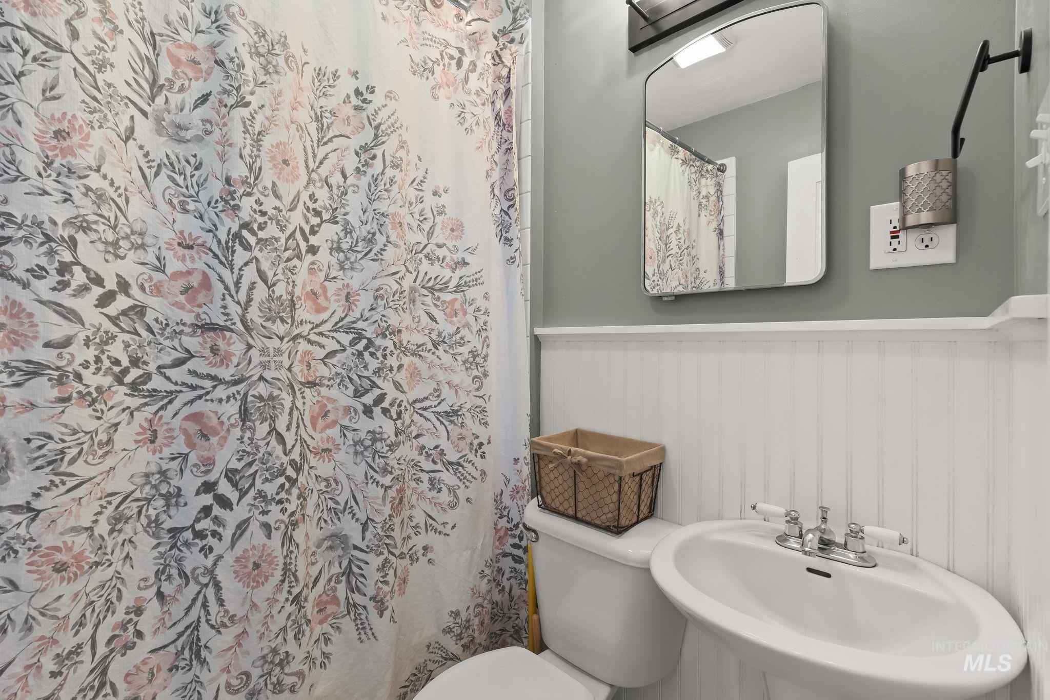 Pedestal sink with chrome faucet, white beadboard wainscoting, and a wall-mounted mirror