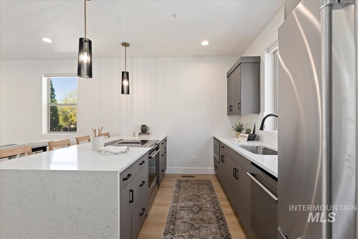 Kitchen with appliances with stainless steel finishes, gray cabinets, light wood finished floors, recessed lighting, and a peninsula