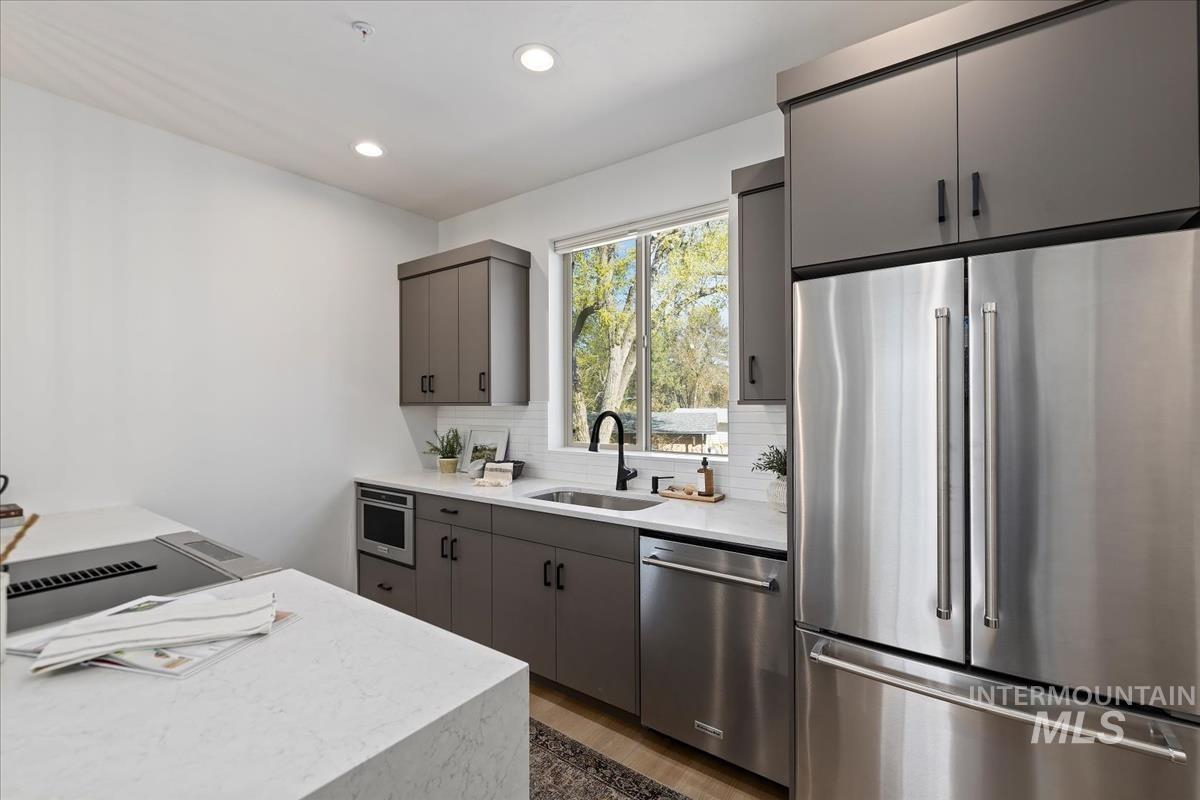 Kitchen with stainless steel appliances, backsplash, recessed lighting, wood finished floors, and gray cabinets