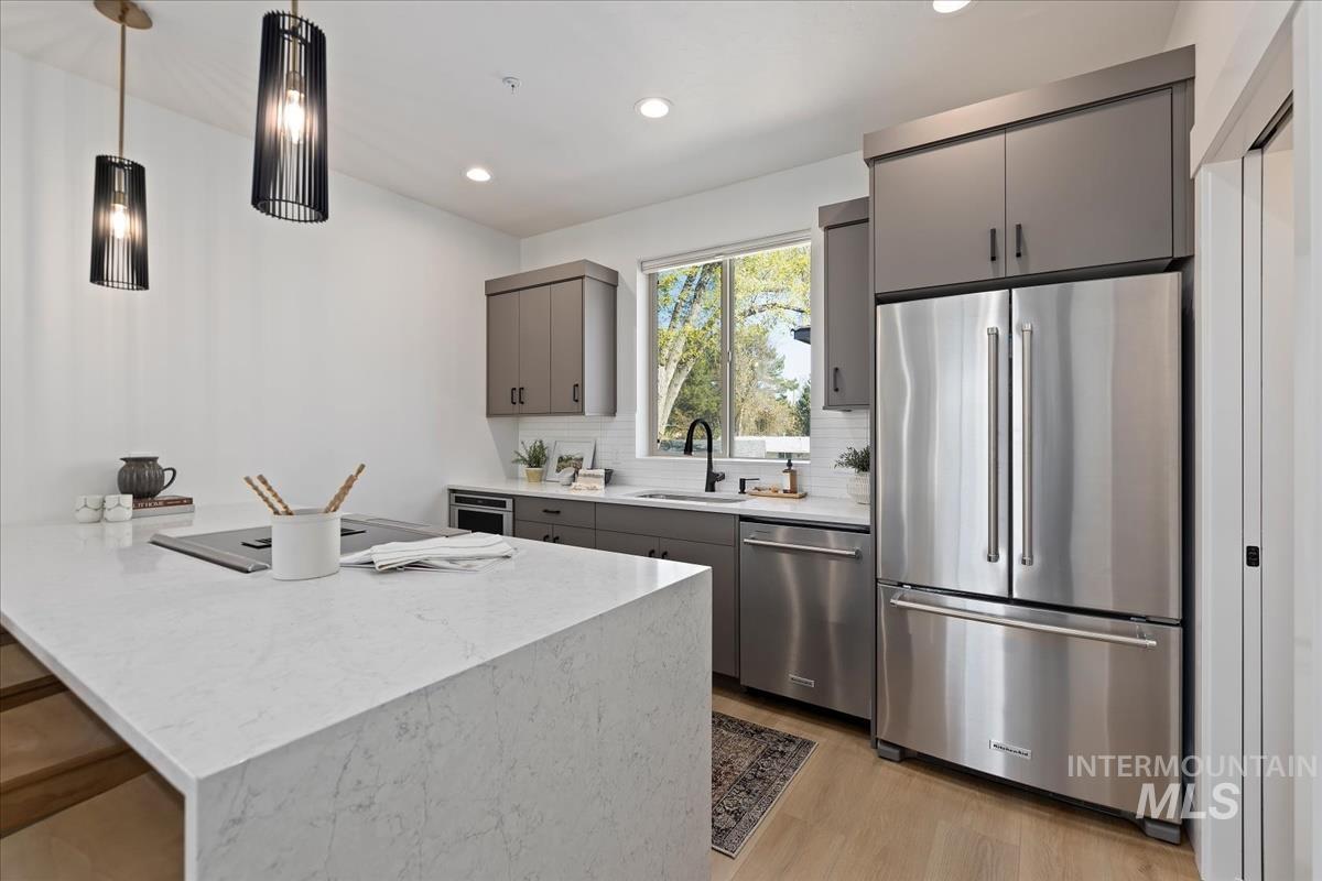 Kitchen featuring stainless steel appliances, gray cabinets, light wood-style flooring, backsplash, and a peninsula