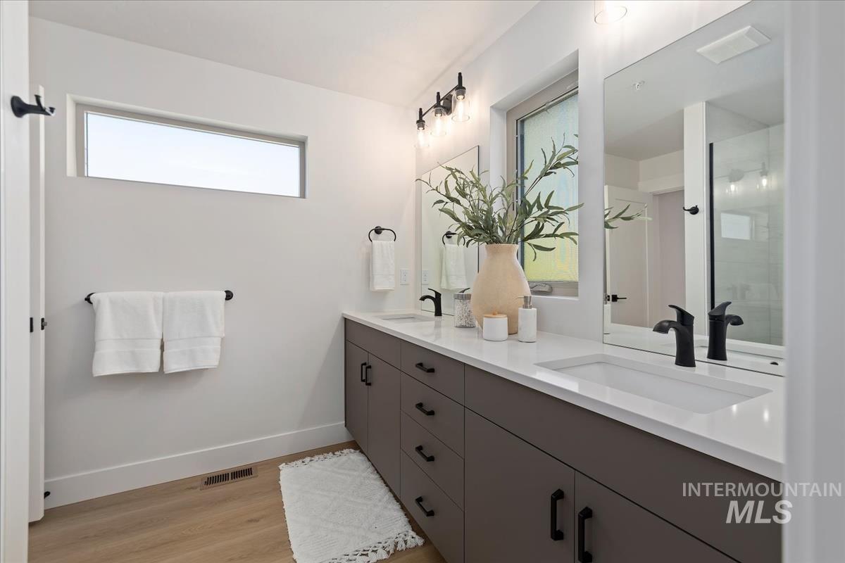 Full bath with double vanity, wood finished floors, and an enclosed shower