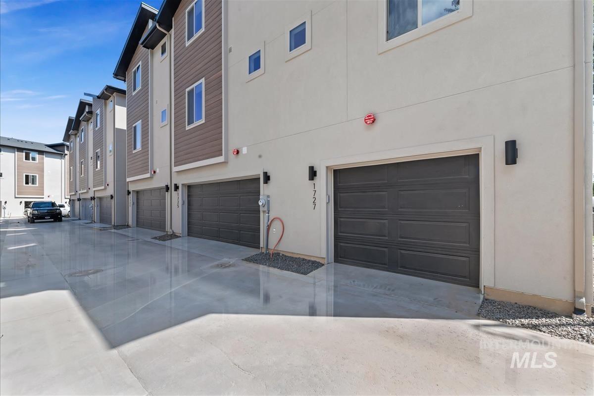 Rear view of house featuring stucco siding, a garage, driveway, and a residential view