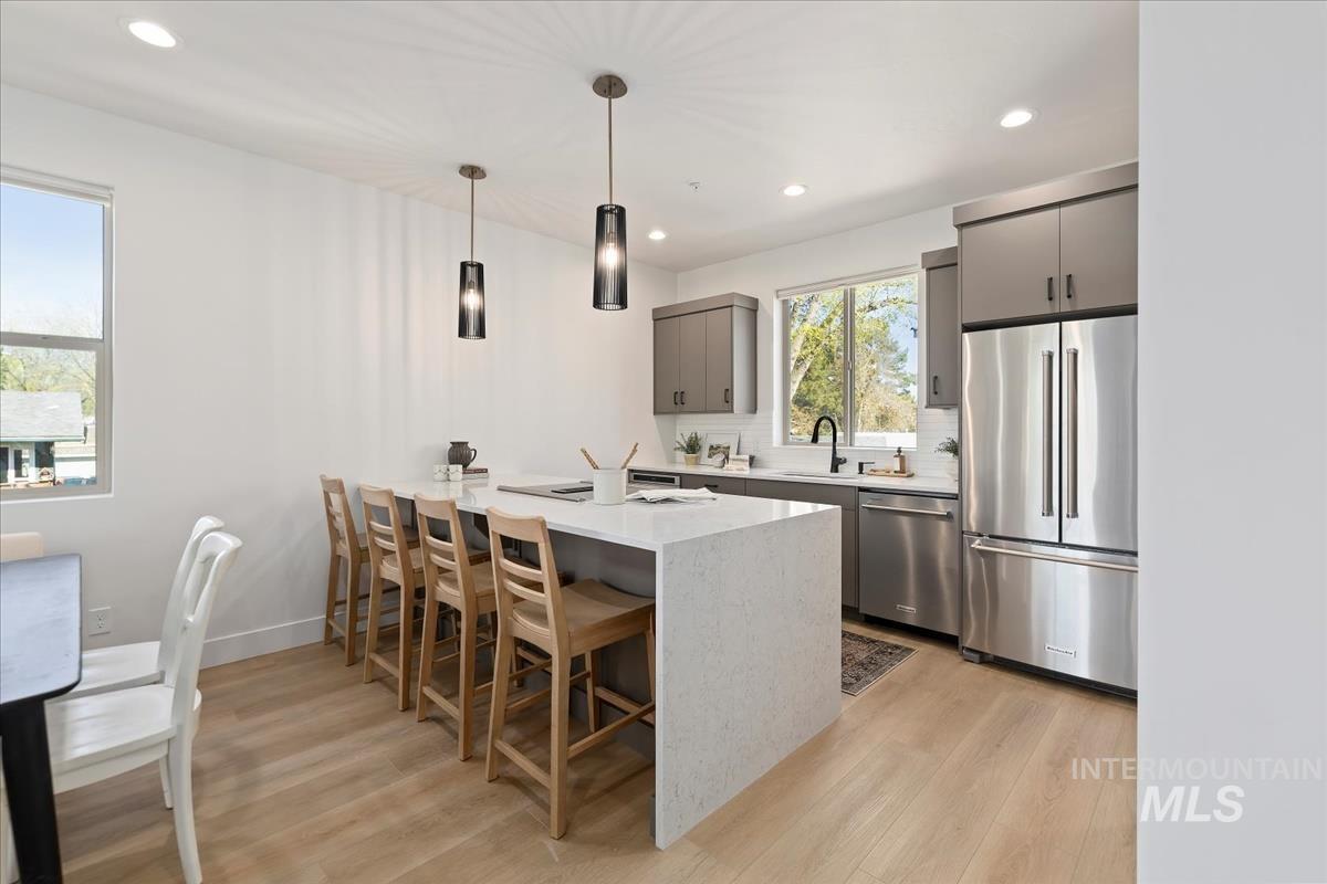 Kitchen featuring stainless steel appliances, light wood-style floors, gray cabinets, a breakfast bar, and recessed lighting