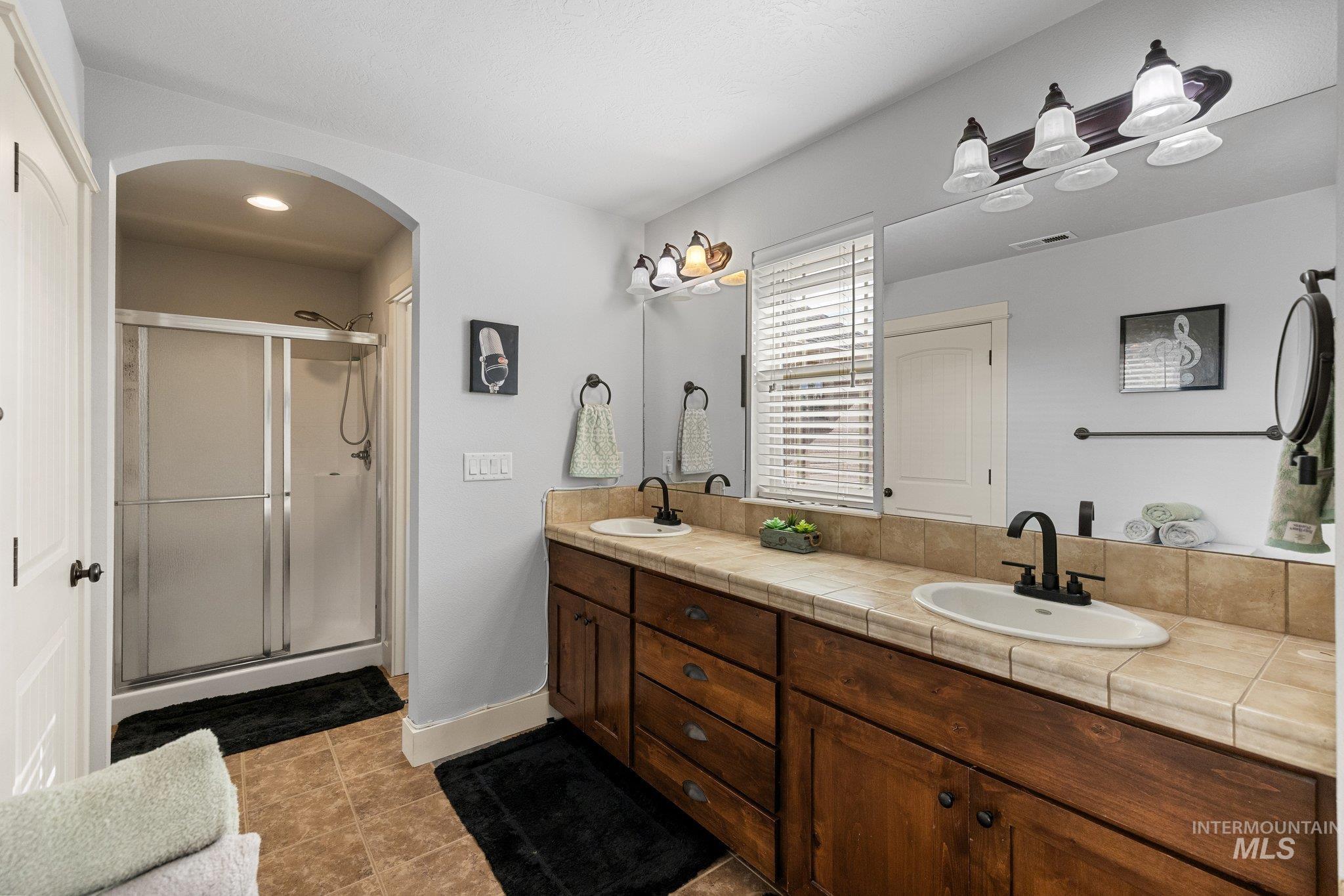 Bathroom featuring double vanity, a shower stall, and dark tile patterned flooring