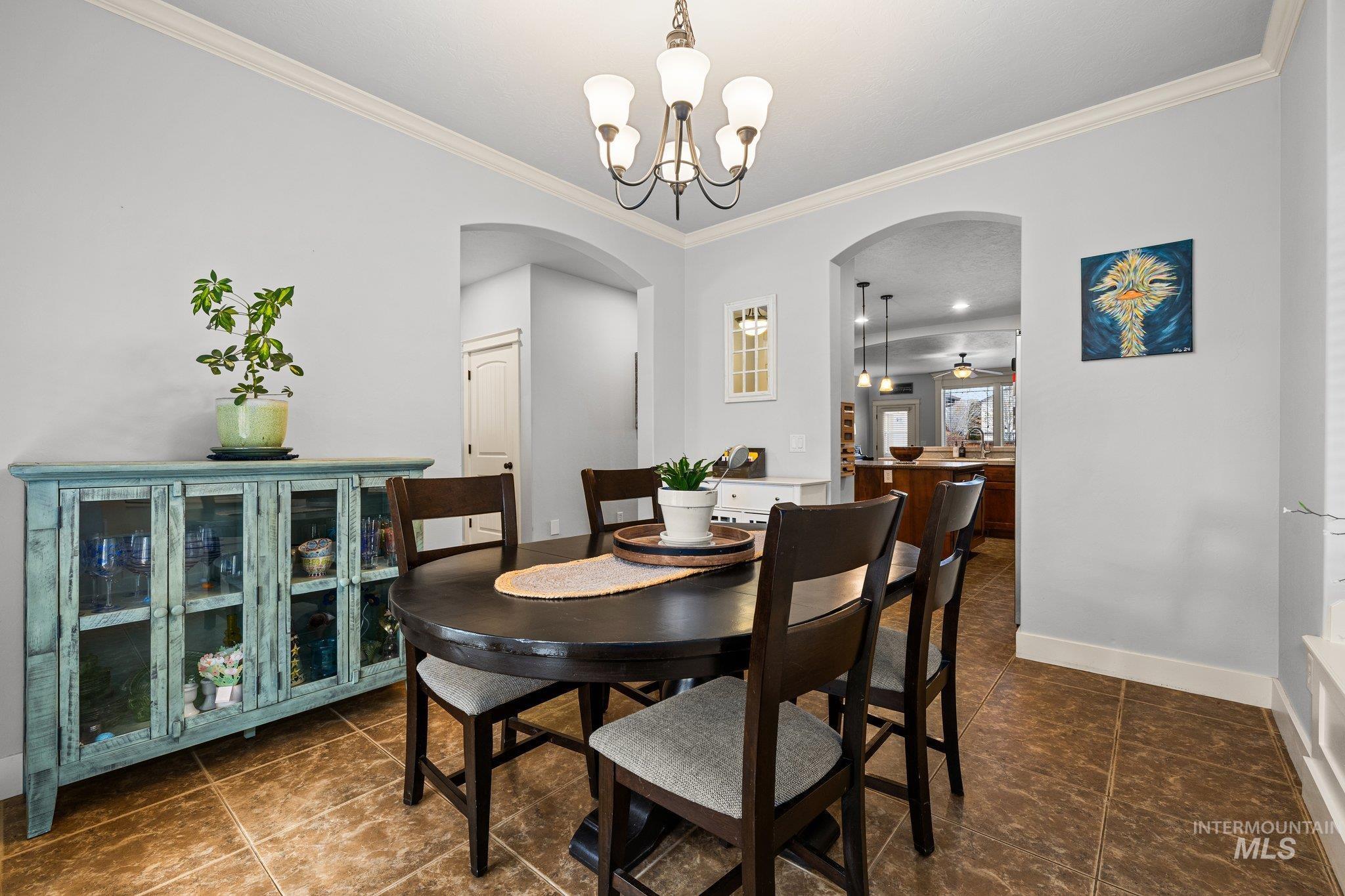 Dining room with arched walkways, crown molding, a chandelier, dark tile patterned floors, and a ceiling fan