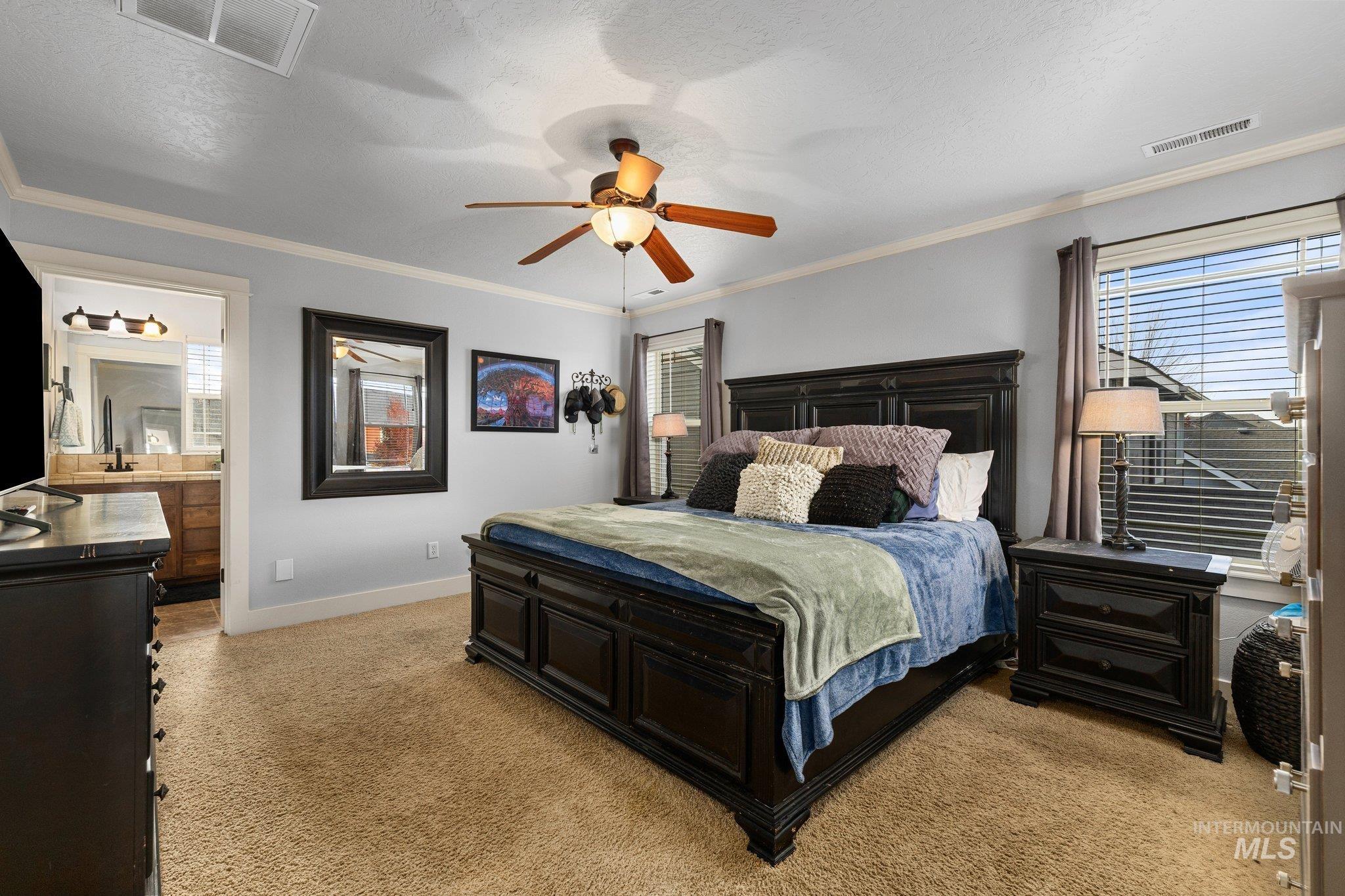 Bedroom with crown molding, light carpet, multiple windows, a textured ceiling, and ceiling fan