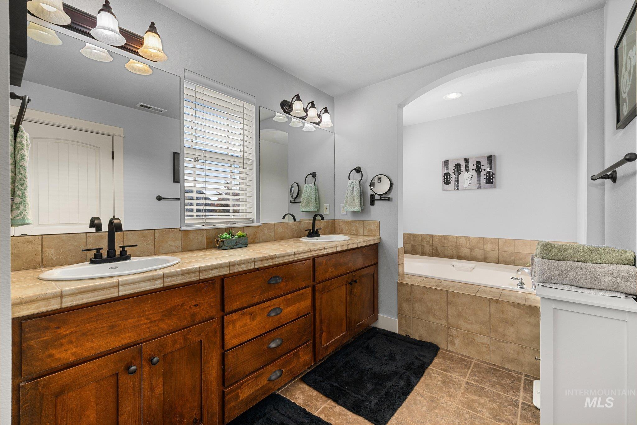 Full bathroom featuring double vanity, a bath, and light tile patterned floors