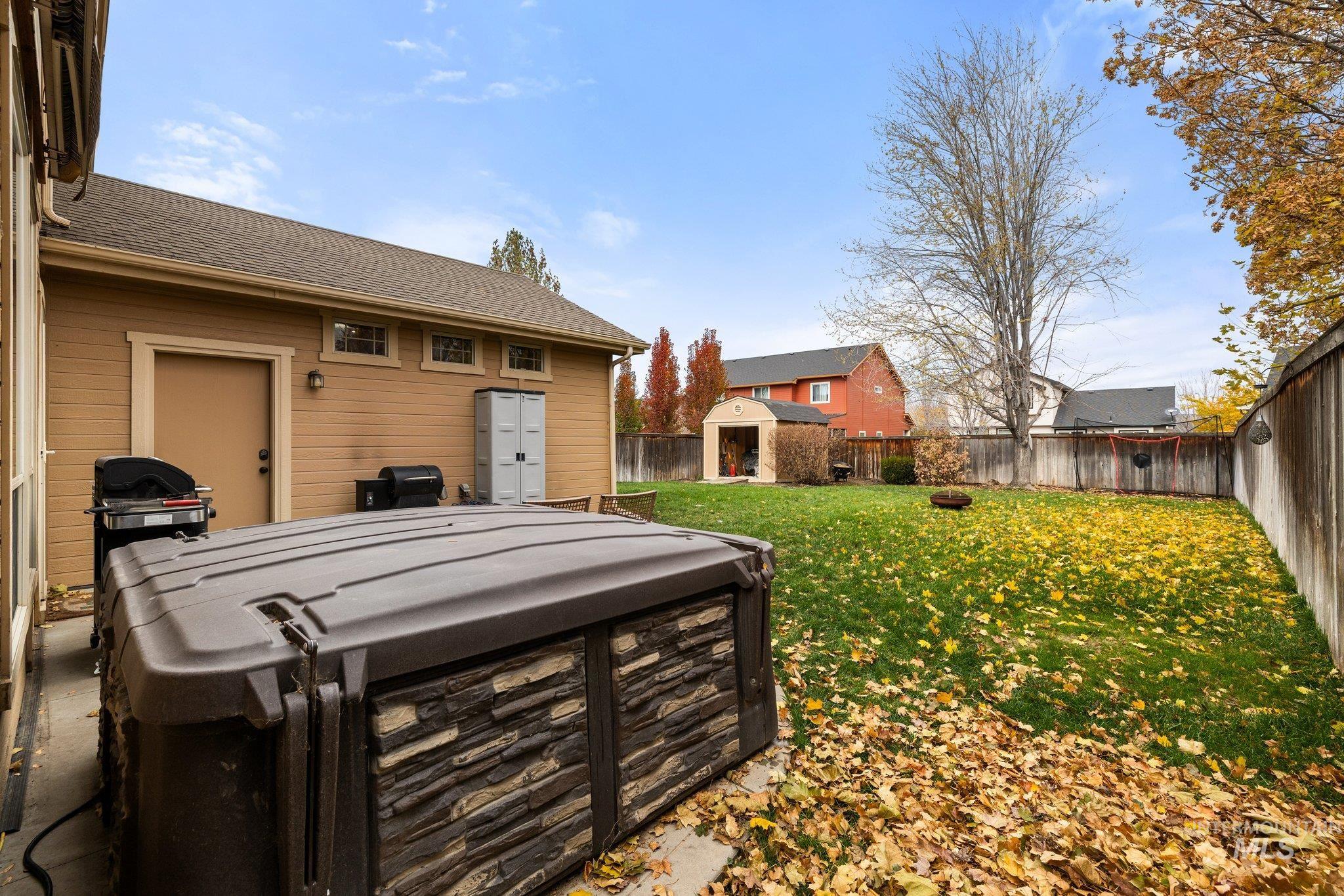Fenced backyard with a patio area, an outbuilding, and a hot tub
