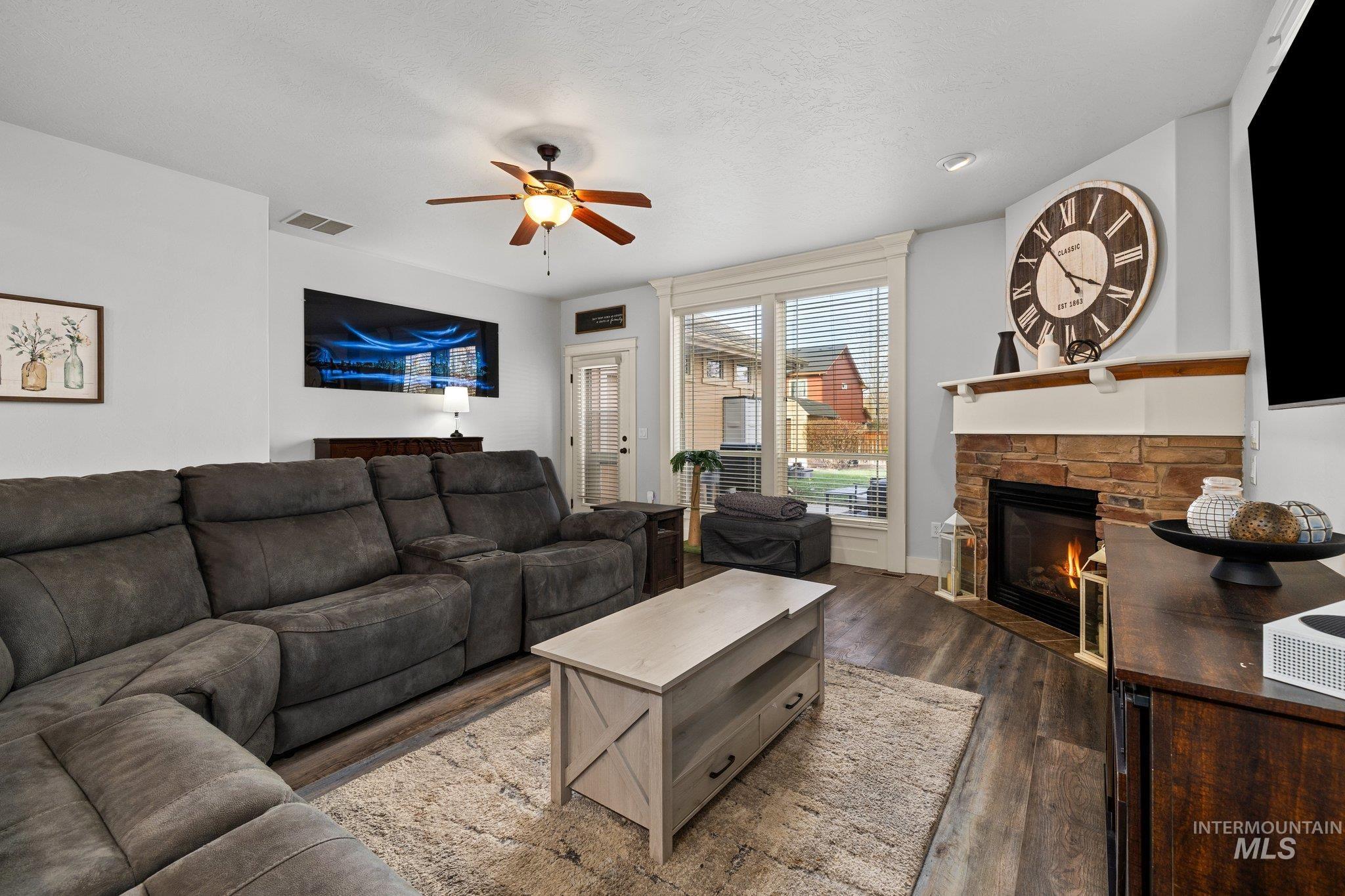 Living area with wood finished floors, a stone fireplace, and ceiling fan