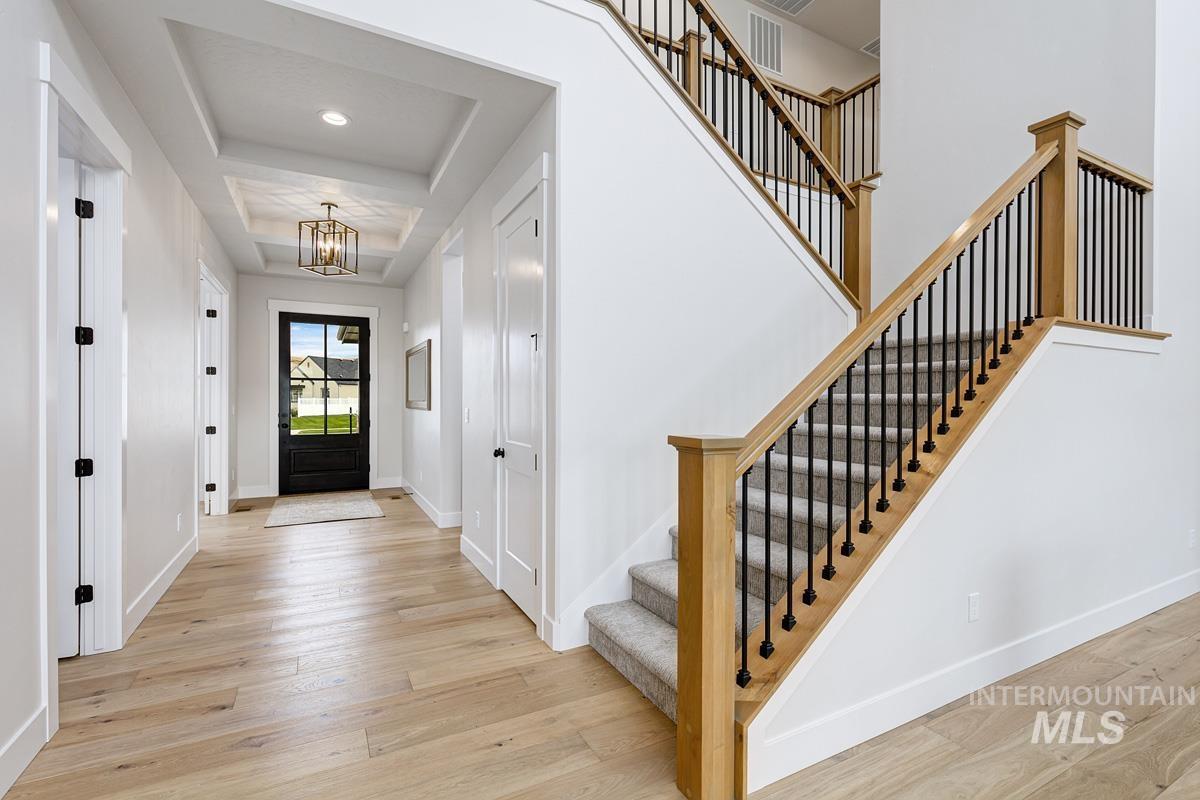 Entrance foyer with light wood-style floors, a chandelier, a raised ceiling, and stairs