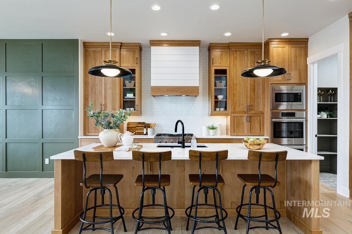 Kitchen with backsplash, brown cabinetry, an island with sink, light wood-style floors, and a breakfast bar area