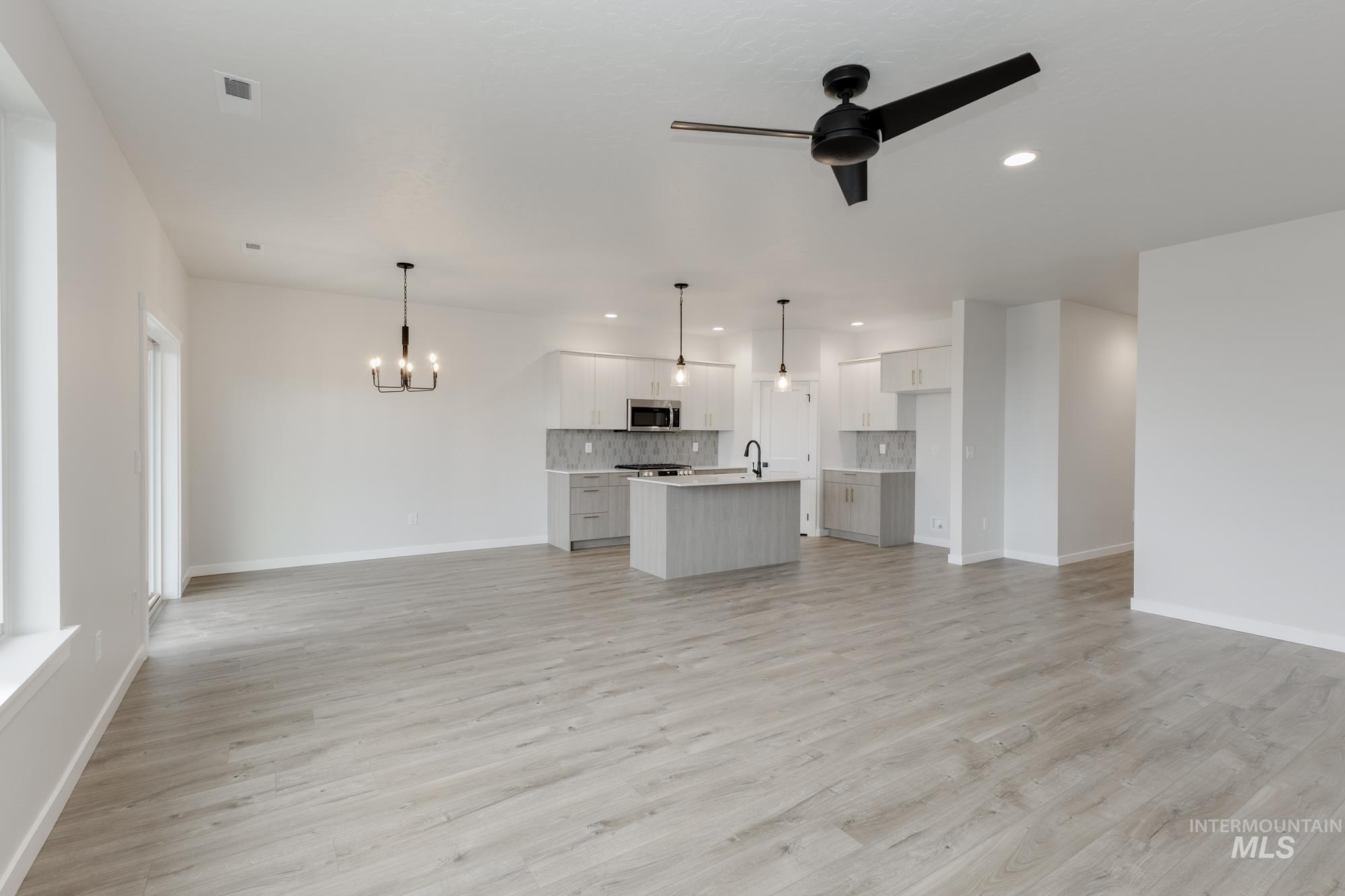 Unfurnished living room featuring a chandelier, light wood finished floors, ceiling fan, and recessed lighting