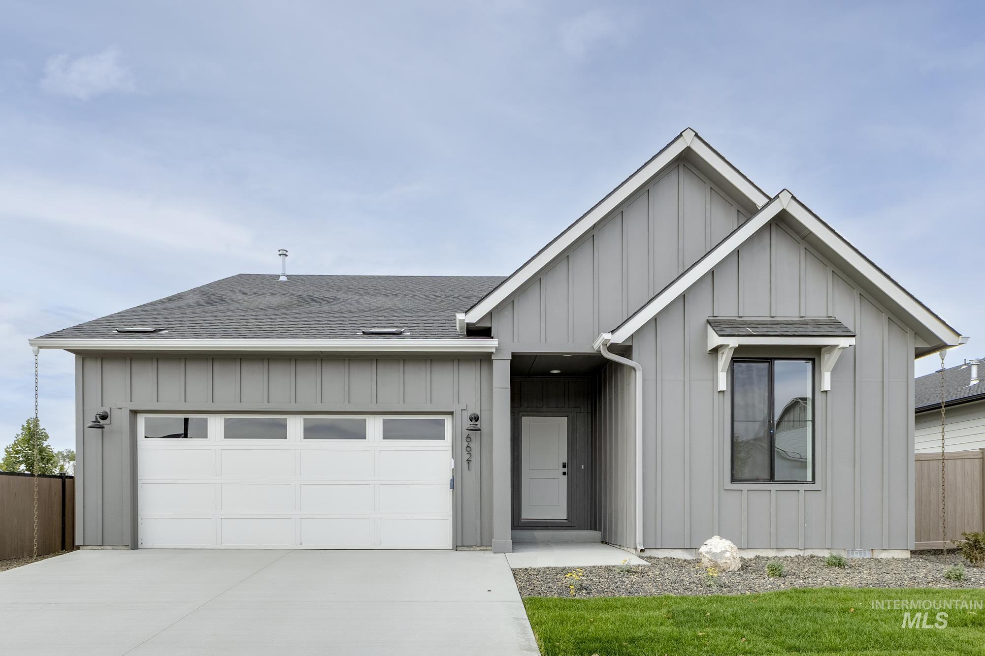 View of front of property with board and batten siding, roof with shingles, an attached garage, and driveway